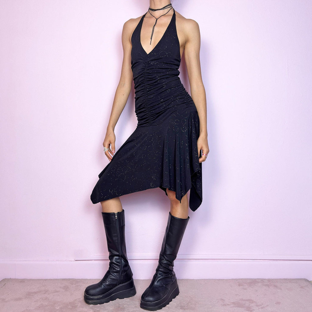 This vintage 2000s black dress features a halter tie neck, deep V-neckline, and allover subtle glitter swirl pattern. The ruched bodice sculpts the waist while the handkerchief hem adds movement and edge. Cut from stretchy fabric with a fluid, body-hugging drape. No closures. A cyber-glam silhouette with clubwear energy—perfect for parties, raves, or statement summer nights. Great vintage condition.