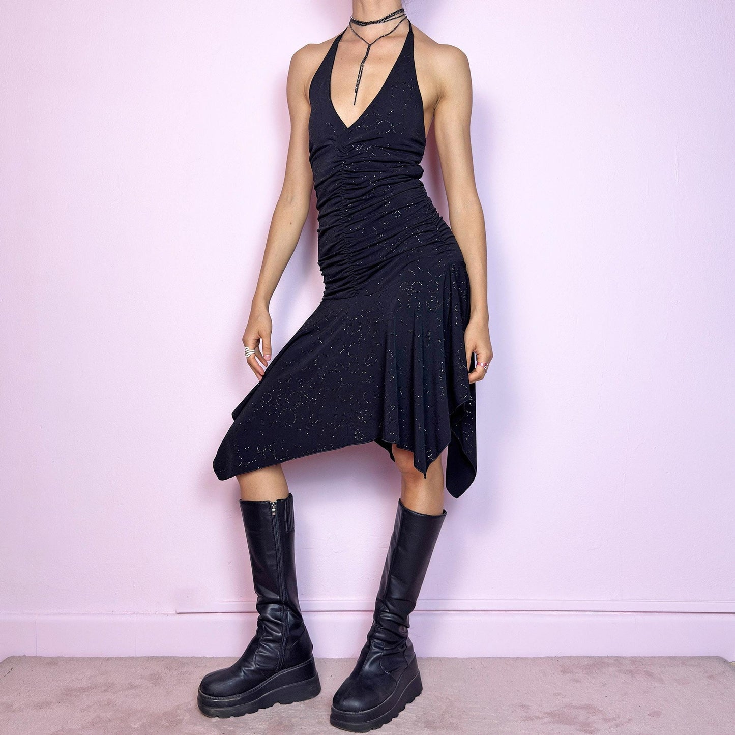 This vintage 2000s black dress features a halter tie neck, deep V-neckline, and allover subtle glitter swirl pattern. The ruched bodice sculpts the waist while the handkerchief hem adds movement and edge. Cut from stretchy fabric with a fluid, body-hugging drape. No closures. A cyber-glam silhouette with clubwear energy—perfect for parties, raves, or statement summer nights. Great vintage condition.