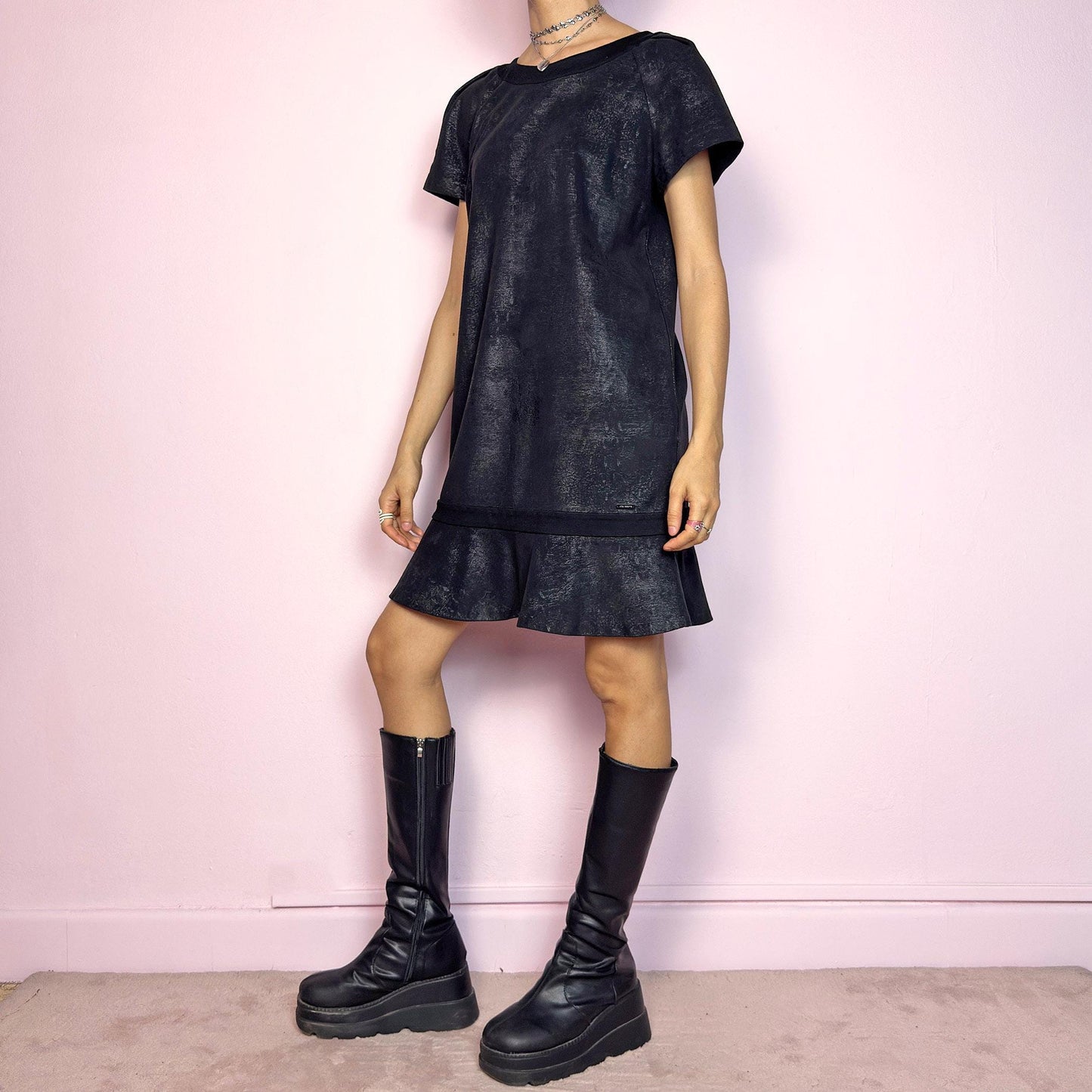 The Y2K Black Cop Copine Dress is a sleek and structured mini dress with subtle futuristic flair. Made from a soft black fabric with a slight sheen and textured abstract finish, it features short sleeves, a relaxed straight silhouette, and a ruffled hem for added movement. The back showcases a bold V-cut detail with a button closure at the neck. Unique yet minimalist, perfect for modern grunge or avant-garde looks. Made in Portugal. Excellent vintage condition.