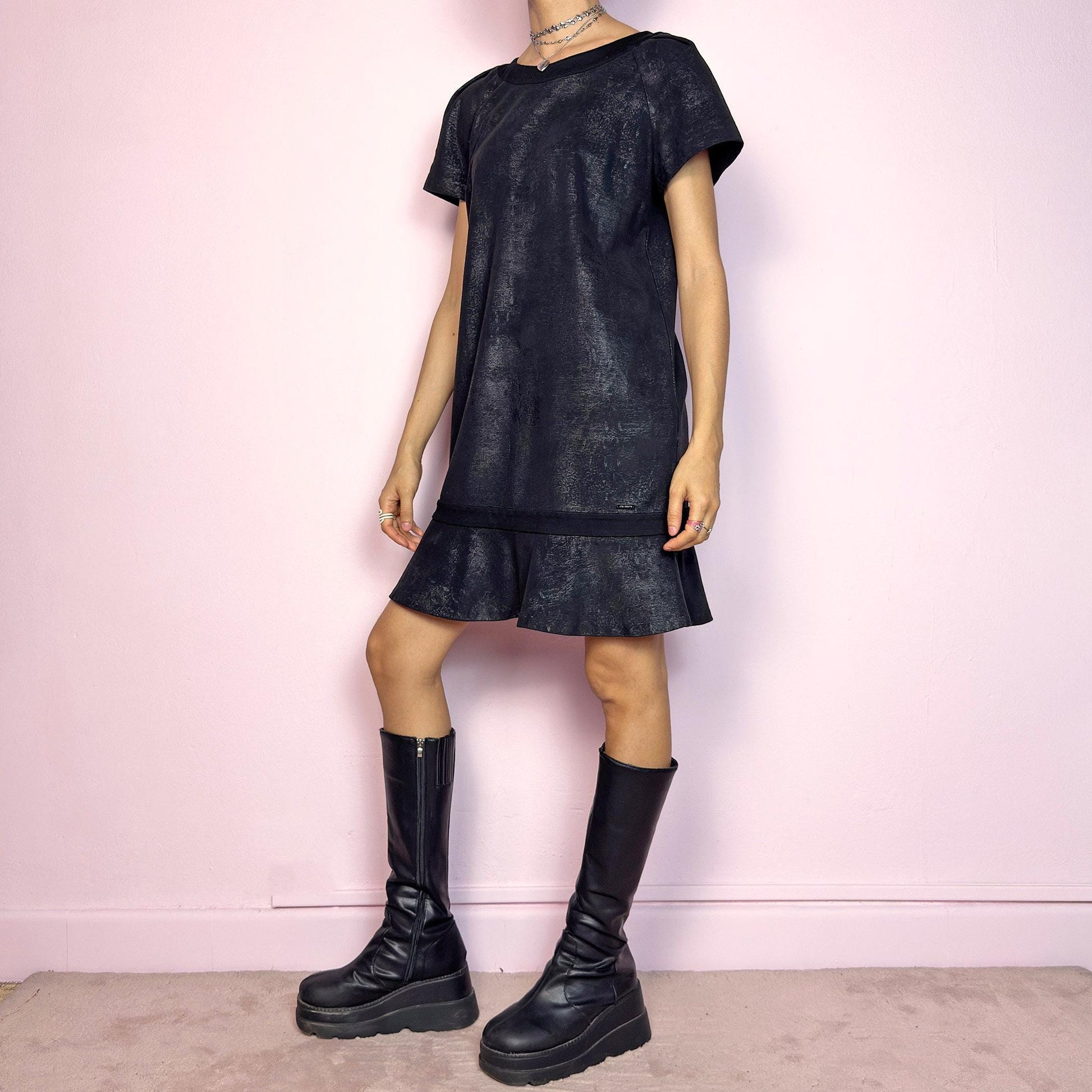 The Y2K Black Cop Copine Dress is a sleek and structured mini dress with subtle futuristic flair. Made from a soft black fabric with a slight sheen and textured abstract finish, it features short sleeves, a relaxed straight silhouette, and a ruffled hem for added movement. The back showcases a bold V-cut detail with a button closure at the neck. Unique yet minimalist, perfect for modern grunge or avant-garde looks. Made in Portugal. Excellent vintage condition.