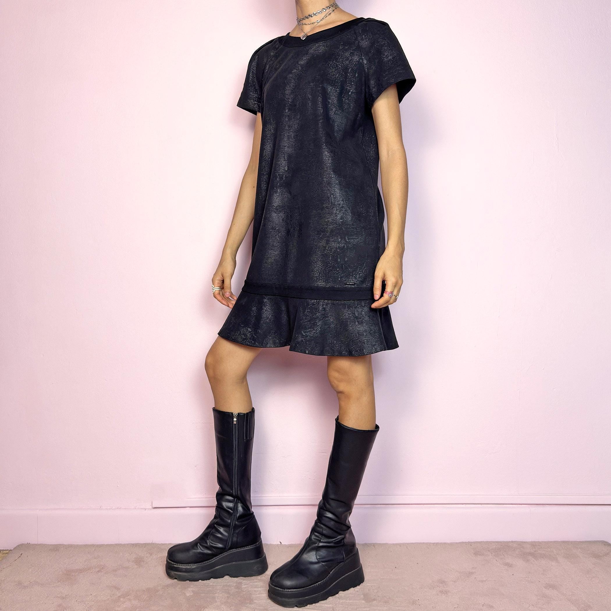 The Y2K Black Cop Copine Dress is a sleek and structured mini dress with subtle futuristic flair. Made from a soft black fabric with a slight sheen and textured abstract finish, it features short sleeves, a relaxed straight silhouette, and a ruffled hem for added movement. The back showcases a bold V-cut detail with a button closure at the neck. Unique yet minimalist, perfect for modern grunge or avant-garde looks. Made in Portugal. Excellent vintage condition.