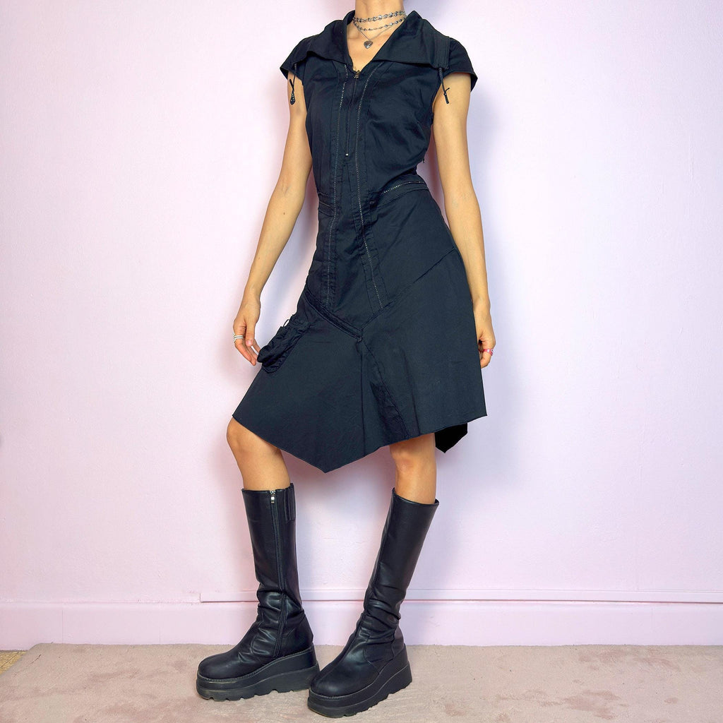 This vintage 2000s black techwear dress features cap sleeves, a dramatic asymmetric hem, and sculptural paneling for a bold silhouette. Made from a stretchy fabric, it includes a side zip closure and ruched utility pocket. Decorative topstitching and a funnel-style collar with drawstrings elevate the structure. Mid-length and lightweight, perfect for summer. A sleek statement in futuristic edge. Great vintage condition.