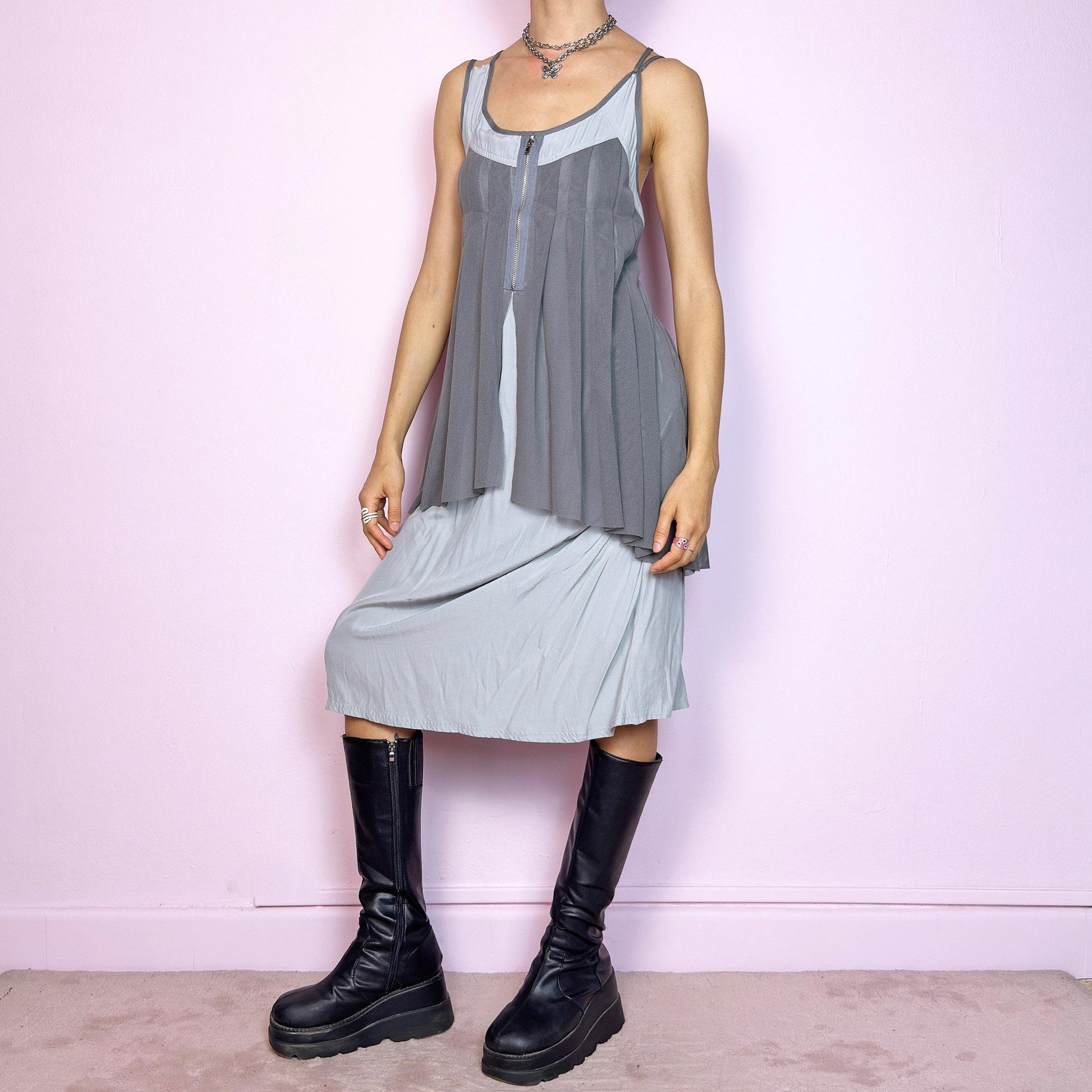 This vintage 2000s midi dress features layered grey tones in mixed textures, including a pleated mesh overlay with faux front zip detail and a side zipper closure. The sleeveless cut and flared asymmetric drape create sculptural movement. Falls below the knee, lightweight, with no stretch. A deconstructed Y2K silhouette—futuristic, quiet, and avant-garde. Perfect for summer days or experimental night looks. Excellent vintage condition.