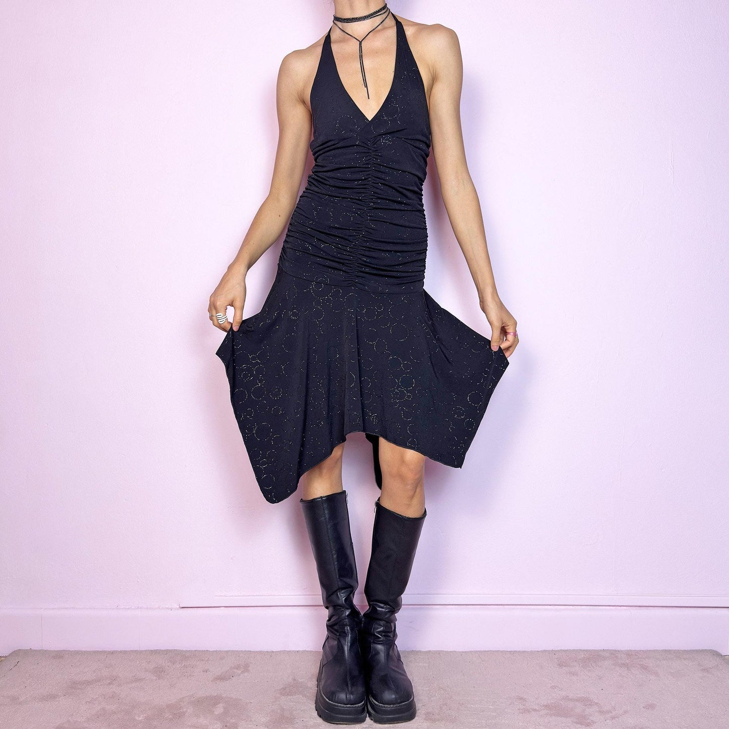 This vintage 2000s black dress features a halter tie neck, deep V-neckline, and allover subtle glitter swirl pattern. The ruched bodice sculpts the waist while the handkerchief hem adds movement and edge. Cut from stretchy fabric with a fluid, body-hugging drape. No closures. A cyber-glam silhouette with clubwear energy—perfect for parties, raves, or statement summer nights. Great vintage condition.