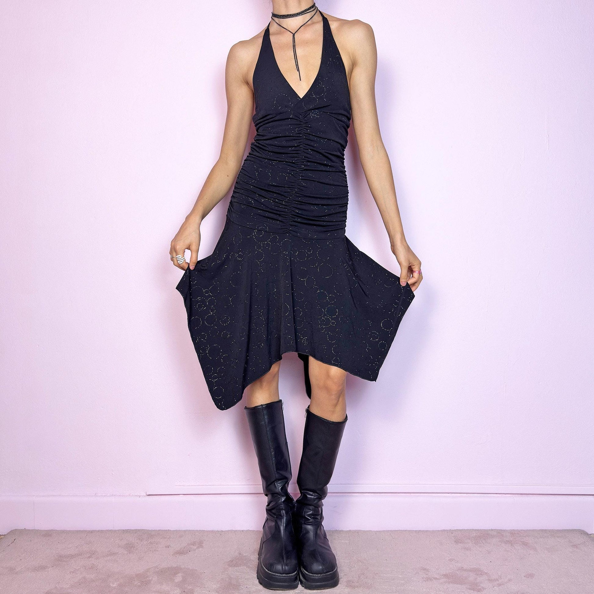 This vintage 2000s black dress features a halter tie neck, deep V-neckline, and allover subtle glitter swirl pattern. The ruched bodice sculpts the waist while the handkerchief hem adds movement and edge. Cut from stretchy fabric with a fluid, body-hugging drape. No closures. A cyber-glam silhouette with clubwear energy—perfect for parties, raves, or statement summer nights. Great vintage condition.