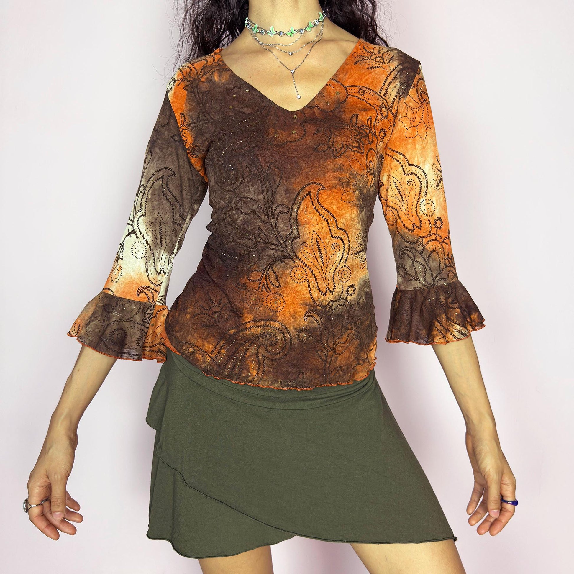 This vintage 2000s mesh top features semi-sheer three-quarter bell sleeves and a deep V-neckline. The fitted silhouette is printed with a burnt orange and brown tie-dye paisley motif, accented by fine gold glitter for subtle shimmer. Made in France, it’s a dreamy piece for romantic, boho, or fairy grunge wardrobes. Made from stretch polyester blend. Excellent vintage condition.