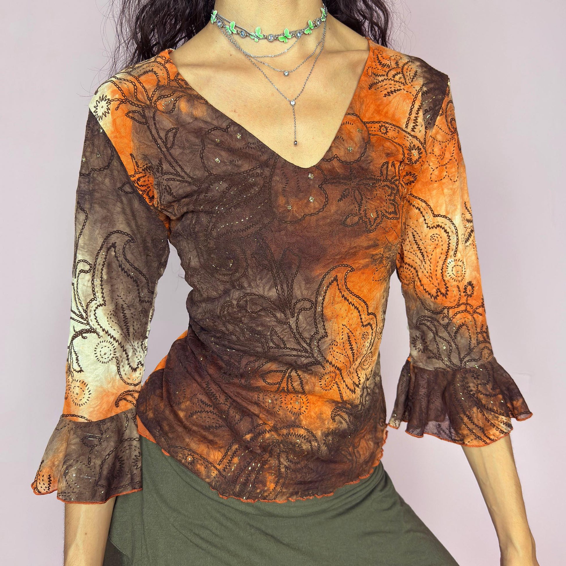 This vintage 2000s mesh top features semi-sheer three-quarter bell sleeves and a deep V-neckline. The fitted silhouette is printed with a burnt orange and brown tie-dye paisley motif, accented by fine gold glitter for subtle shimmer. Made in France, it’s a dreamy piece for romantic, boho, or fairy grunge wardrobes. Made from stretch polyester blend. Excellent vintage condition.