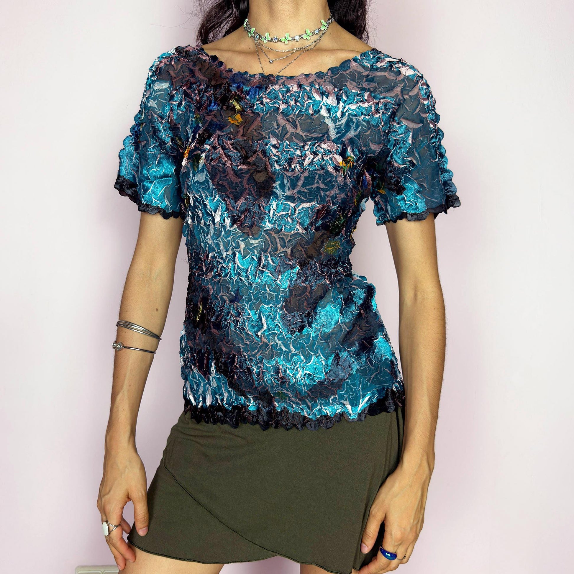 This vintage 90s avant-garde semi-sheer crinkle mesh top shimmers in shiny shades of teal, navy, and plum, with hints of white highlights. The pleated texture and short sleeves evoke playful elegance. Ideal for night outs, art parties, or expressive layering. A rare archival piece with pictorial, painterly brushstroke detail. Made of lightweight stretch fabric. Excellent vintage condition.