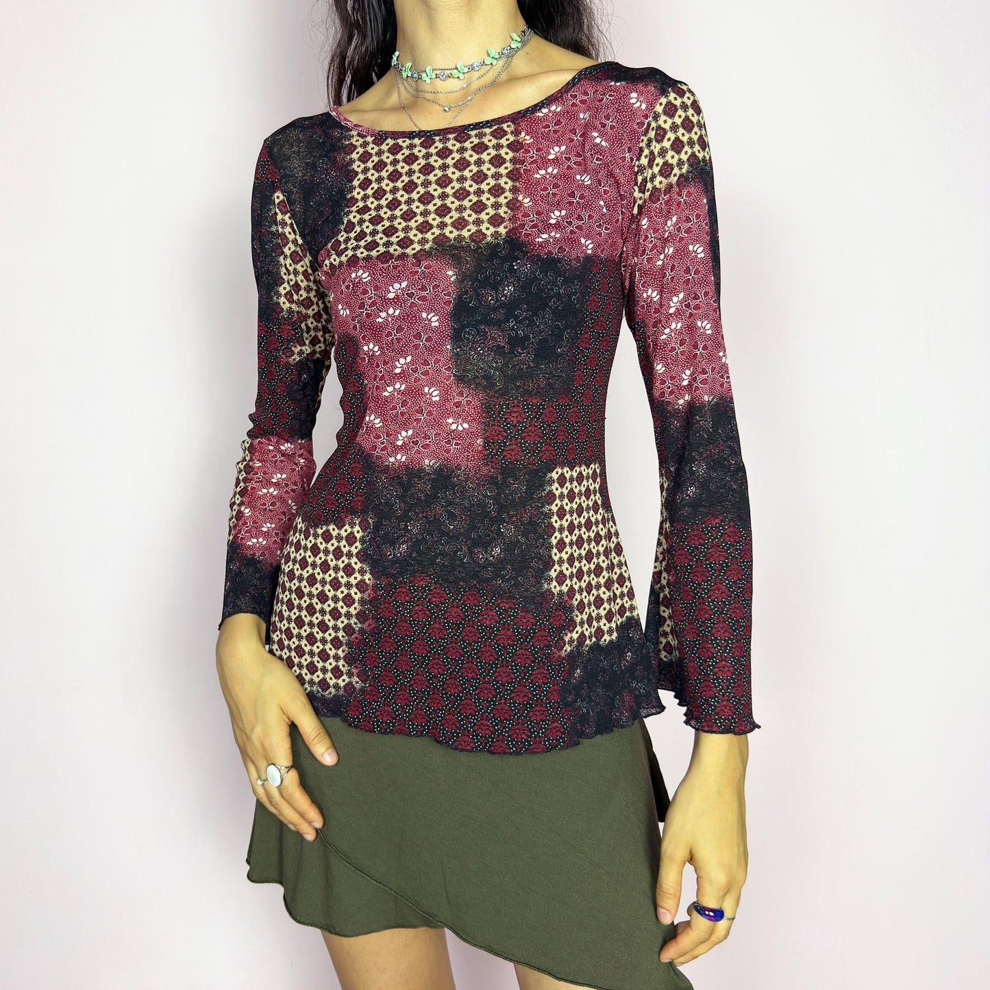 This vintage 2000s mesh top features bracelet-length bell sleeves and a patchwork floral print in burgundy, black, and beige tones. The fitted silhouette and lettuce hem add delicate structure to its ethereal mood. Ideal for witchy autumn layering or spring evening parties. A romantic, whimsical Y2K piece. Made of stretch polyester. Excellent vintage condition.