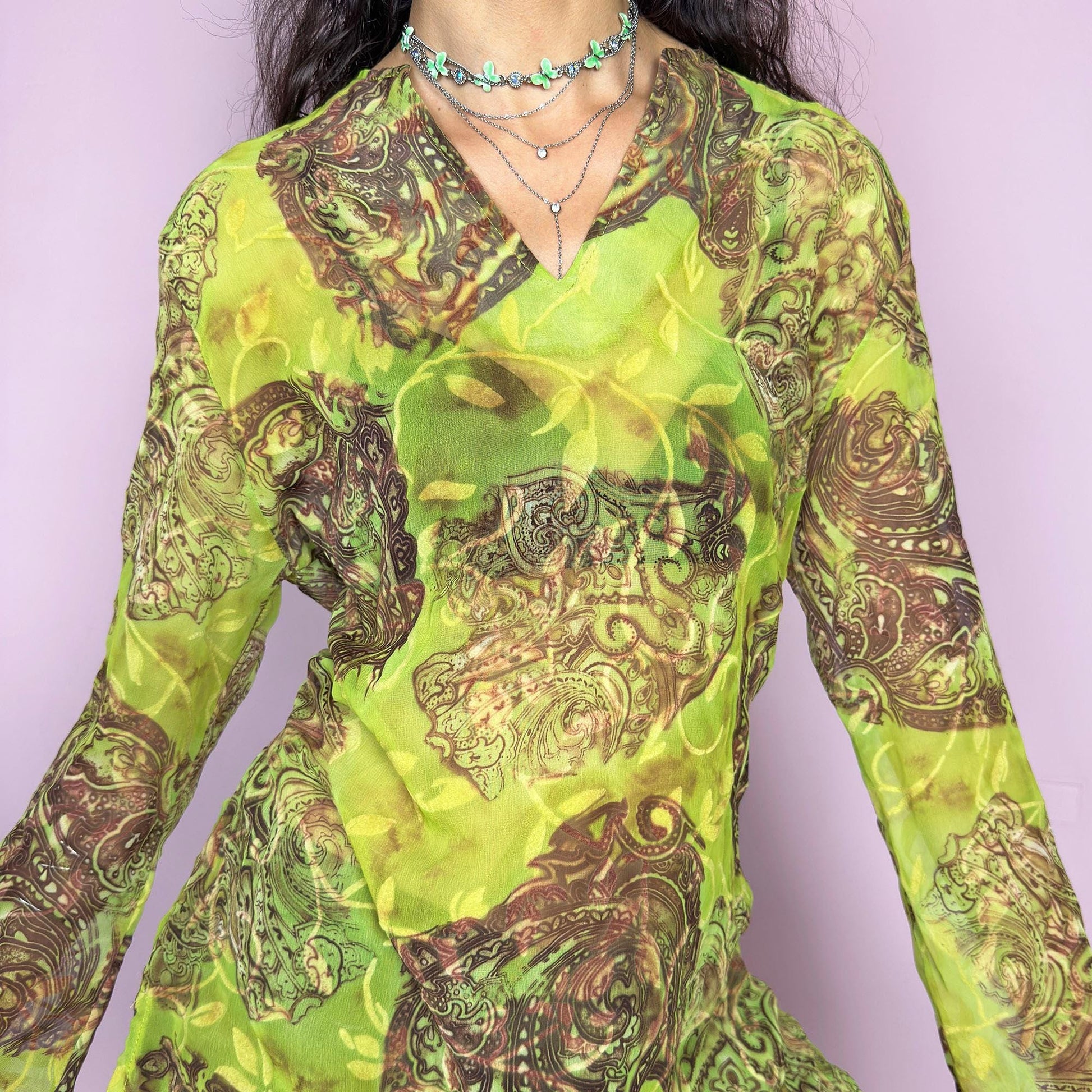 This vintage 2000s bohemian sheer green blouse casts a psychedelic glow with swirling brown paisley motifs and fluid draping. Flared long sleeves and a soft V-neckline evoke carefree elegance. Wear it layered at summer parties or as a lightweight, kaftan-inspired beach cover-up. Made in France from lightweight polyester. Excellent vintage condition.