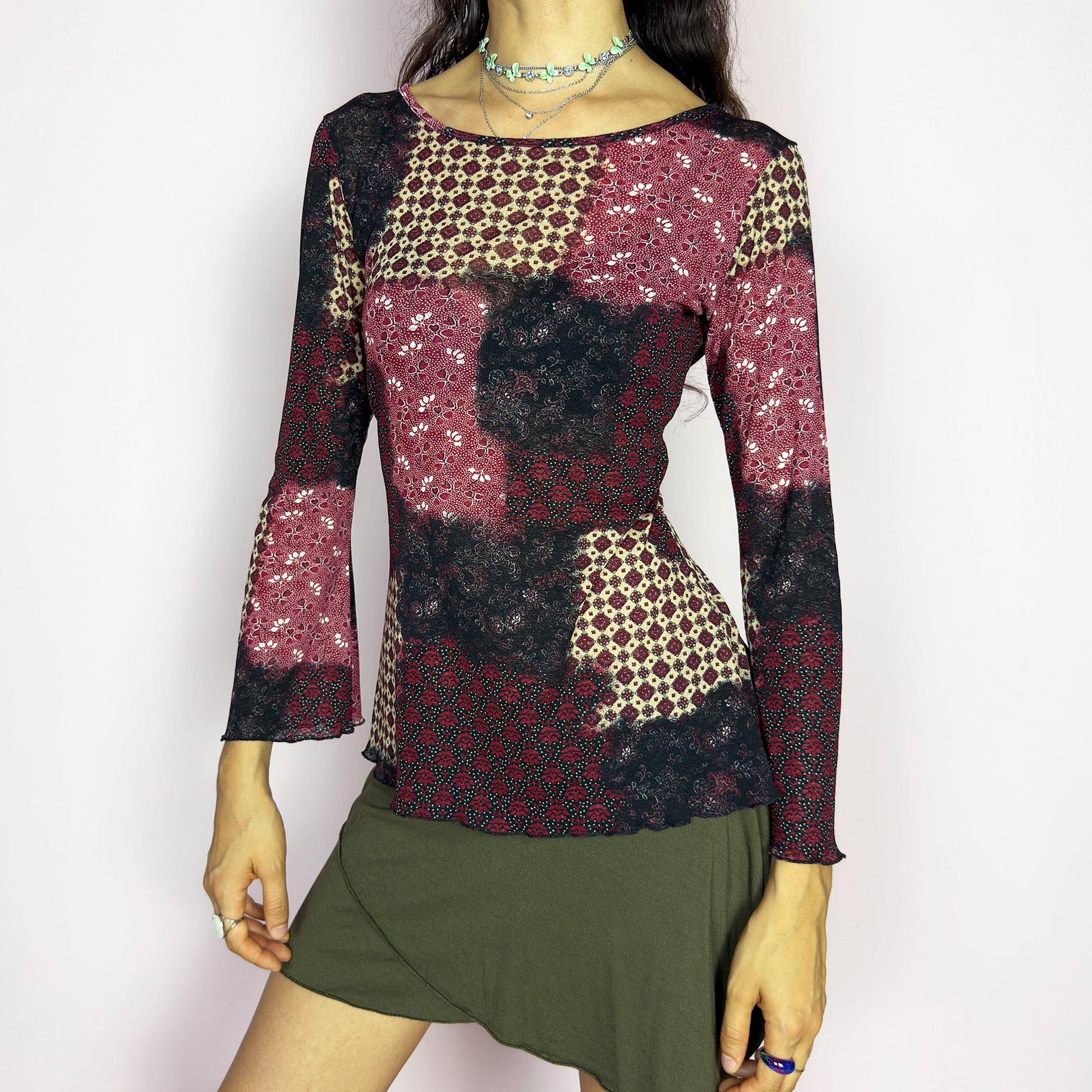 This vintage 2000s mesh top features bracelet-length bell sleeves and a patchwork floral print in burgundy, black, and beige tones. The fitted silhouette and lettuce hem add delicate structure to its ethereal mood. Ideal for witchy autumn layering or spring evening parties. A romantic, whimsical Y2K piece. Made of stretch polyester. Excellent vintage condition.