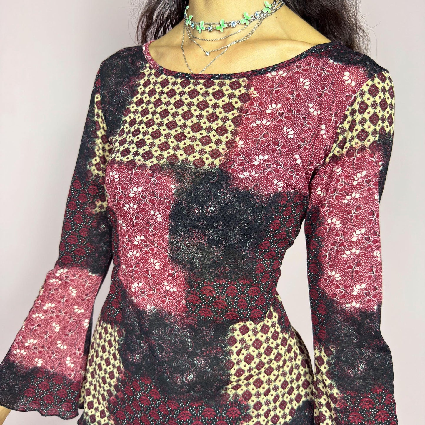This vintage 2000s mesh top features bracelet-length bell sleeves and a patchwork floral print in burgundy, black, and beige tones. The fitted silhouette and lettuce hem add delicate structure to its ethereal mood. Ideal for witchy autumn layering or spring evening parties. A romantic, whimsical Y2K piece. Made of stretch polyester. Excellent vintage condition.