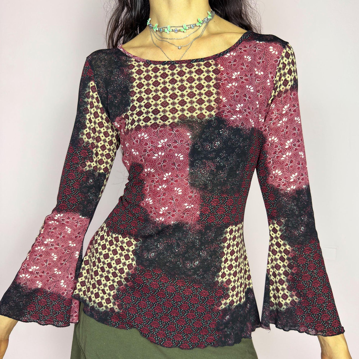 This vintage 2000s mesh top features bracelet-length bell sleeves and a patchwork floral print in burgundy, black, and beige tones. The fitted silhouette and lettuce hem add delicate structure to its ethereal mood. Ideal for witchy autumn layering or spring evening parties. A romantic, whimsical Y2K piece. Made of stretch polyester. Excellent vintage condition.