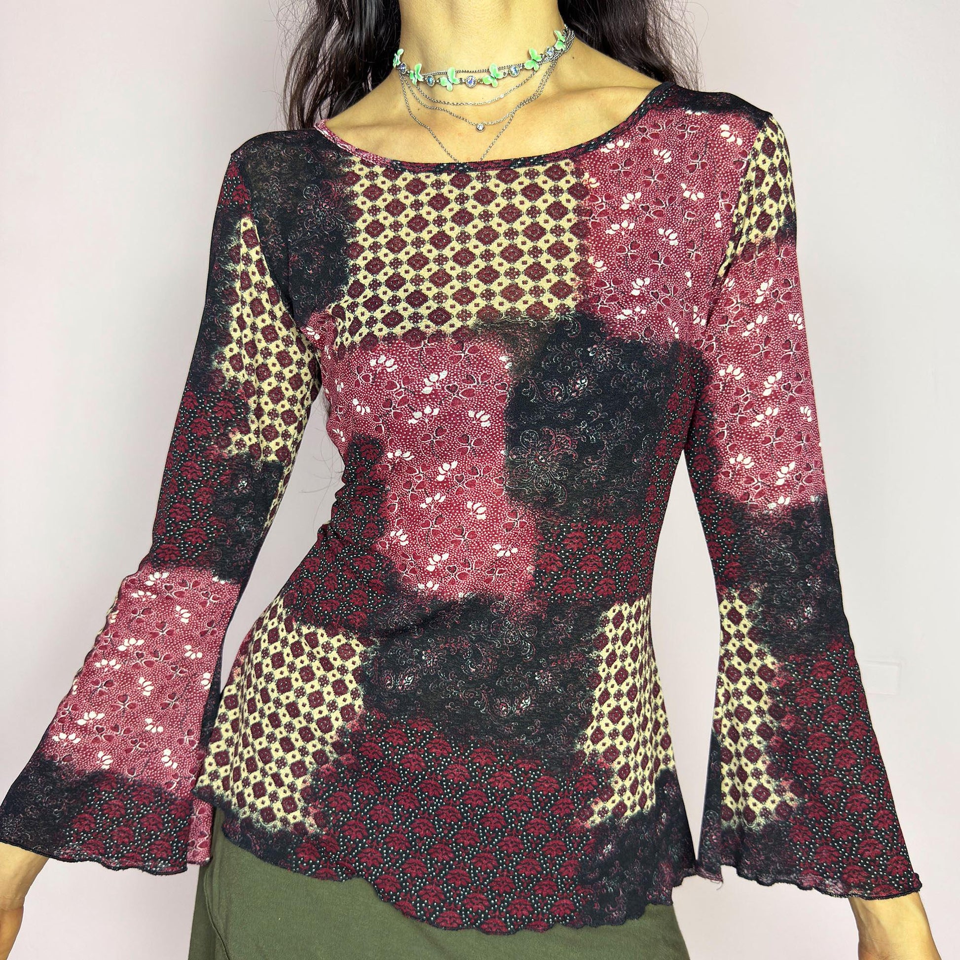 This vintage 2000s mesh top features bracelet-length bell sleeves and a patchwork floral print in burgundy, black, and beige tones. The fitted silhouette and lettuce hem add delicate structure to its ethereal mood. Ideal for witchy autumn layering or spring evening parties. A romantic, whimsical Y2K piece. Made of stretch polyester. Excellent vintage condition.