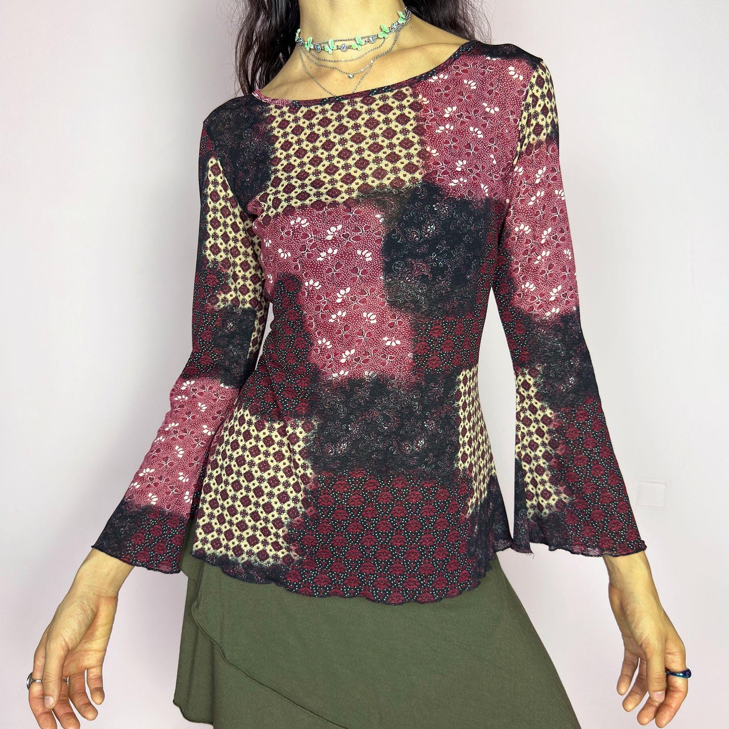 This vintage 2000s mesh top features bracelet-length bell sleeves and a patchwork floral print in burgundy, black, and beige tones. The fitted silhouette and lettuce hem add delicate structure to its ethereal mood. Ideal for witchy autumn layering or spring evening parties. A romantic, whimsical Y2K piece. Made of stretch polyester. Excellent vintage condition.