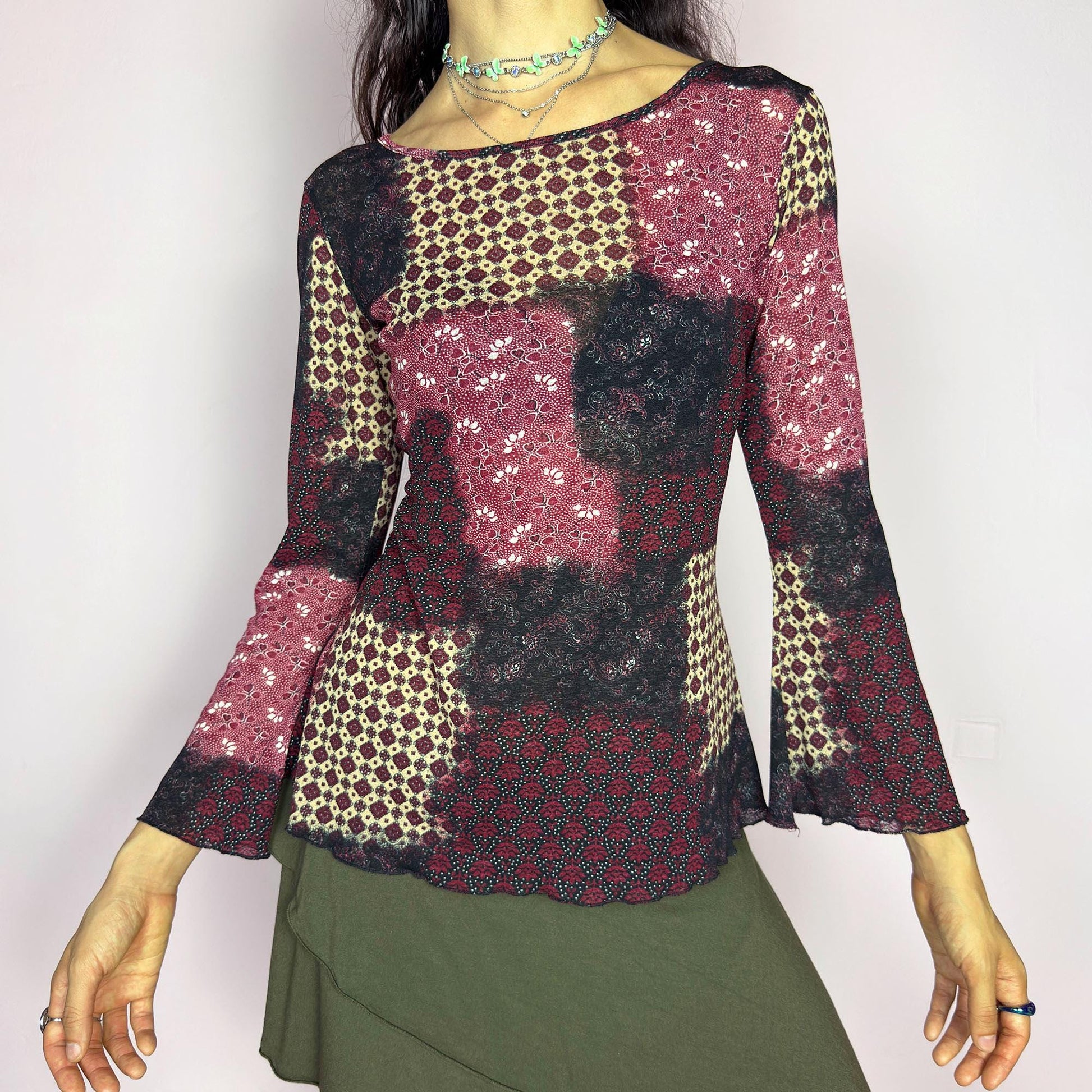 This vintage 2000s mesh top features bracelet-length bell sleeves and a patchwork floral print in burgundy, black, and beige tones. The fitted silhouette and lettuce hem add delicate structure to its ethereal mood. Ideal for witchy autumn layering or spring evening parties. A romantic, whimsical Y2K piece. Made of stretch polyester. Excellent vintage condition.