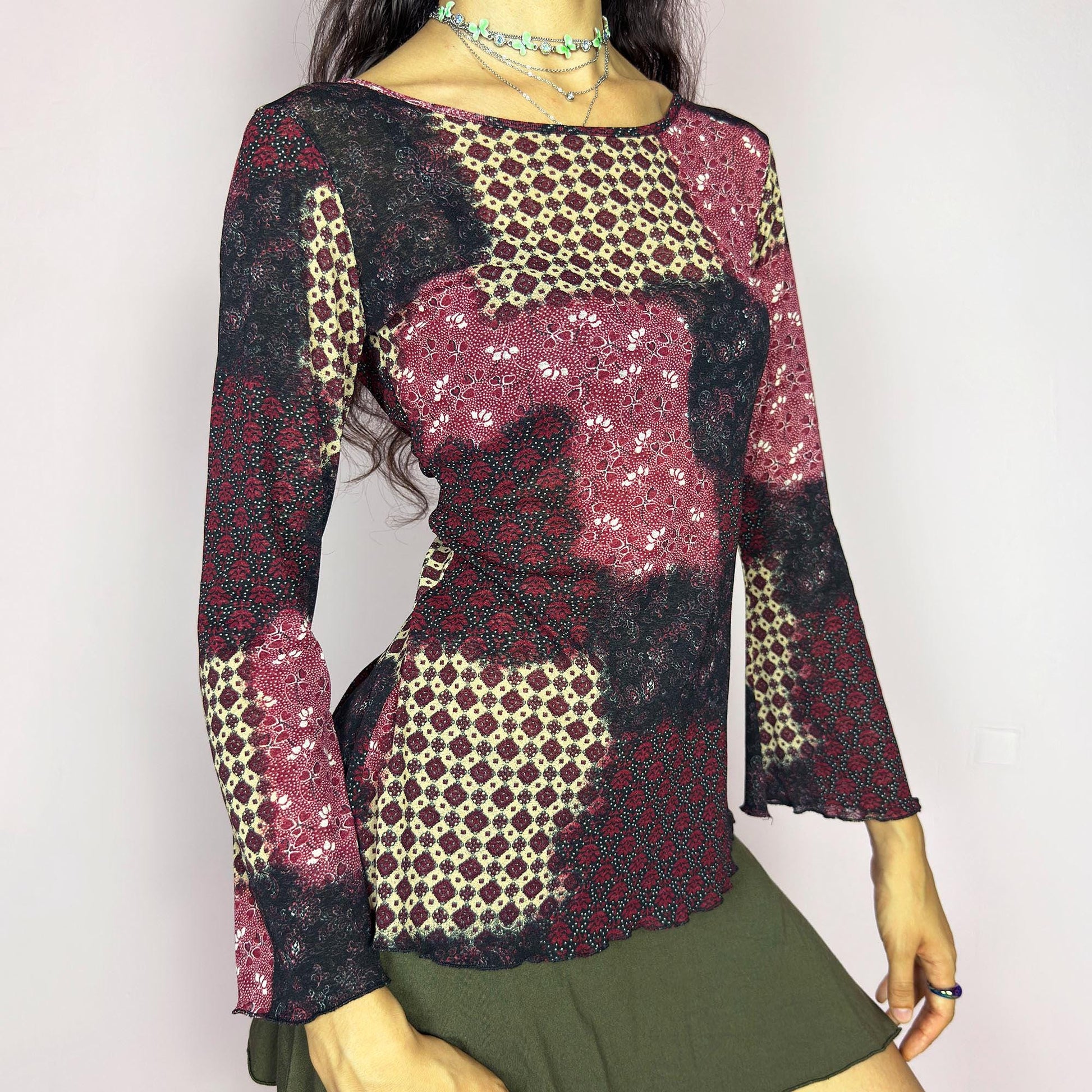 This vintage 2000s mesh top features bracelet-length bell sleeves and a patchwork floral print in burgundy, black, and beige tones. The fitted silhouette and lettuce hem add delicate structure to its ethereal mood. Ideal for witchy autumn layering or spring evening parties. A romantic, whimsical Y2K piece. Made of stretch polyester. Excellent vintage condition.