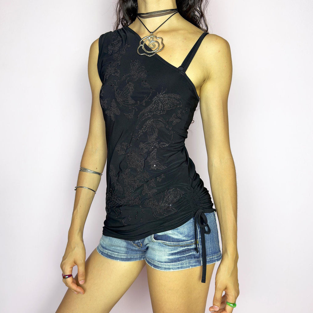 The Y2K Black Sequin Butterfly Top is a vintage 2000s asymmetrical design featuring glittery butterfly motifs, ruched sides, and dual drawstring ties at the shoulder and hem. Crafted from stretchy black fabric with a body-skimming fit, it blends glam detail with subversive edge. Ideal for party nights, clubbing, or iconic festival looks. A millennium-era classic with bold, sculptural energy. Great vintage condition.