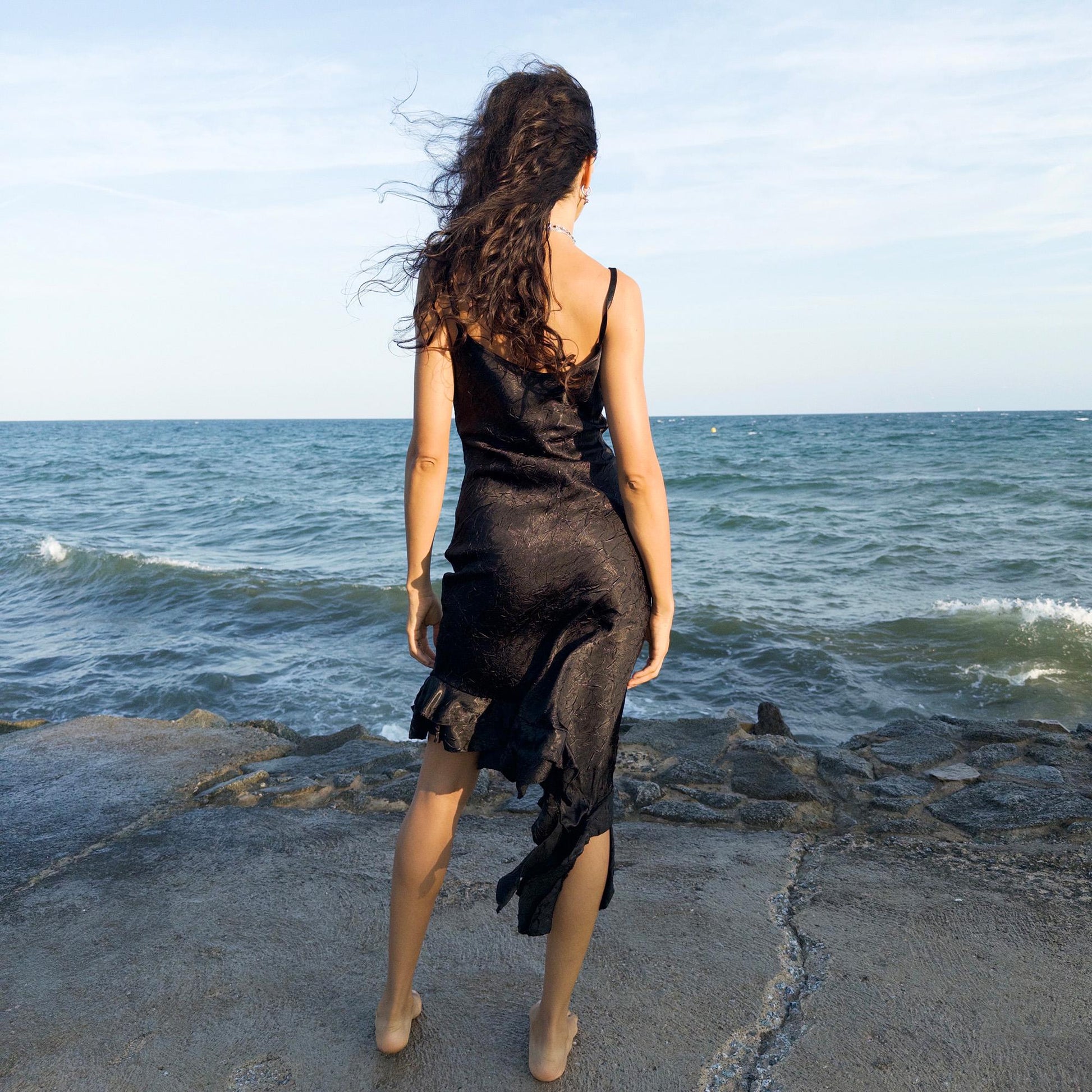 The vintage 2000s black slip dress is a made-in-France piece with crinkled texture and asymmetric ruffle hem. Its sculptural midi silhouette moves with quiet sensuality—ideal for gallery openings, formal nights, or late summer dates. A deconstructed Y2K shape that evokes avant-garde elegance, made to be seen without shouting. An archival dress crafted from a soft polyester blend. Excellent vintage condition.