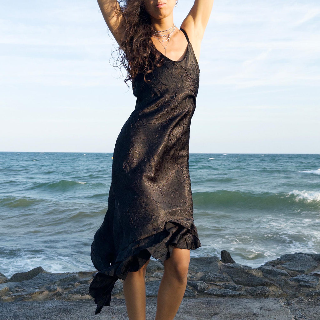 The vintage 2000s black slip dress is a made-in-France piece with crinkled texture and asymmetric ruffle hem. Its sculptural midi silhouette moves with quiet sensuality—ideal for gallery openings, formal nights, or late summer dates. A deconstructed Y2K shape that evokes avant-garde elegance, made to be seen without shouting. An archival dress crafted from a soft polyester blend. Excellent vintage condition.
