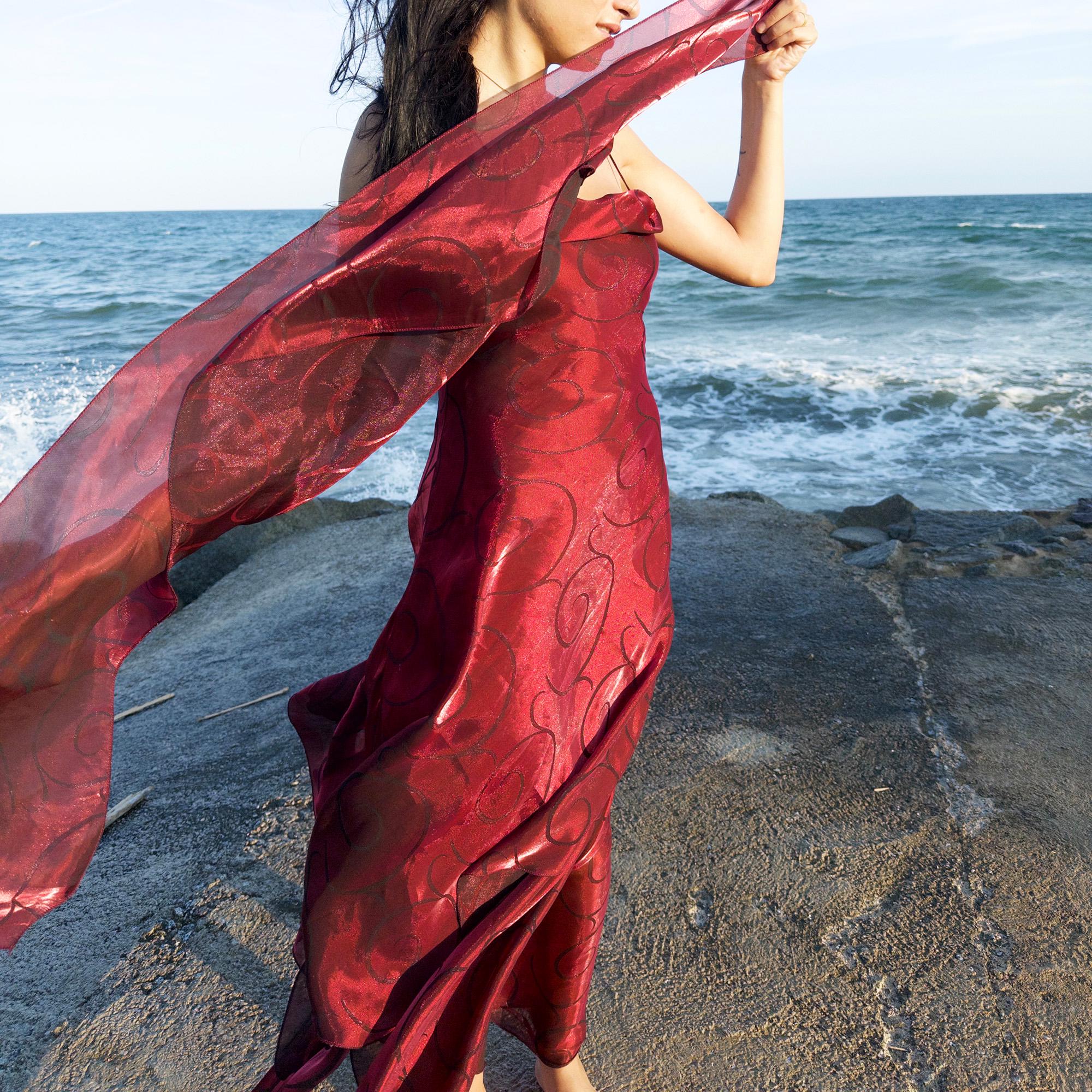 The vintage 2000s red organza-style slip midi dress is a French-made evening piece with layered maroon tones and tonal swirl pattern. With delicate spaghetti straps, side zip, and a flowing asymmetrical hem, it includes a matching scarf. Ideal for galas, proms, or romantic nights under open skies. Crafted from a semi-sheer, non-stretch fabric. Excellent vintage condition.