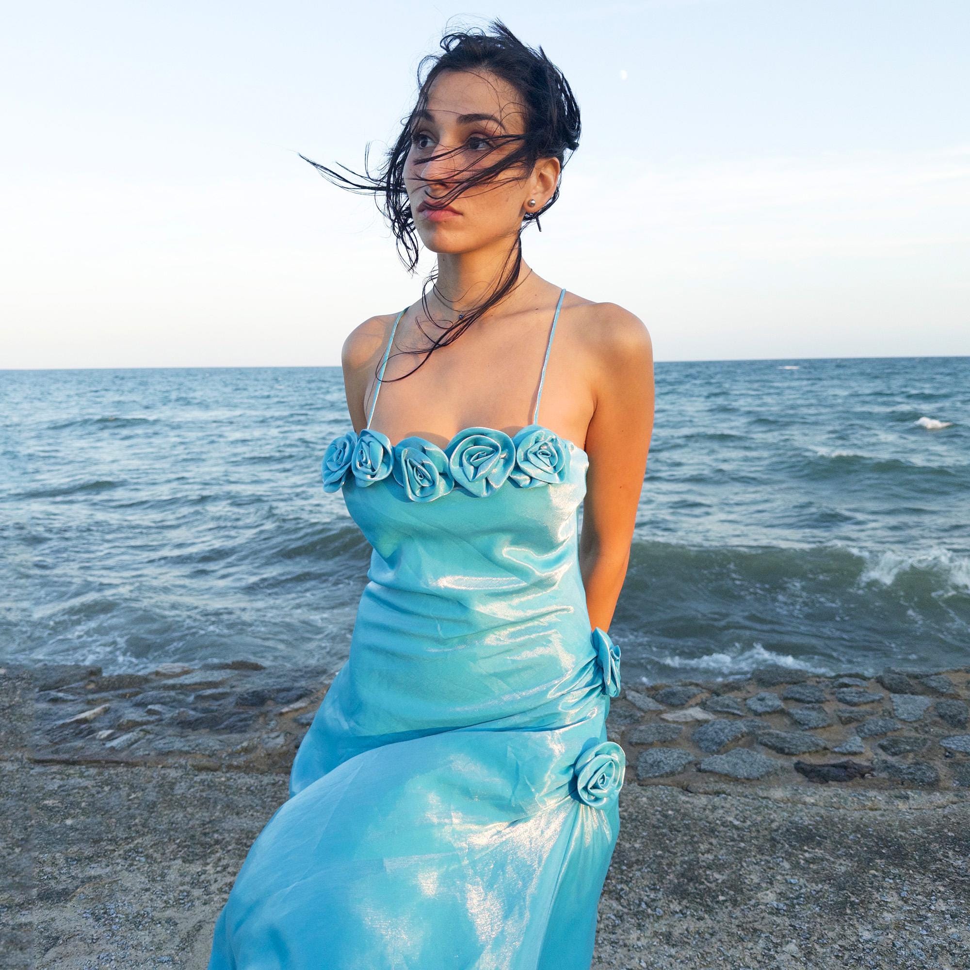 The vintage 2000s blue slip dress is a French-made fantasy with sculptural rosette appliqué along the bust and ruched side detail. Its iridescent finish and fluid midi length evoke a dreamy softness, perfect for proms, summer weddings, or romantic evenings. The silhouette is both delicate and structured, capturing quiet glamour with fairytale allure. A romantic Y2K archive crafted from a shimmering non-stretch fabric. Great vintage condition.