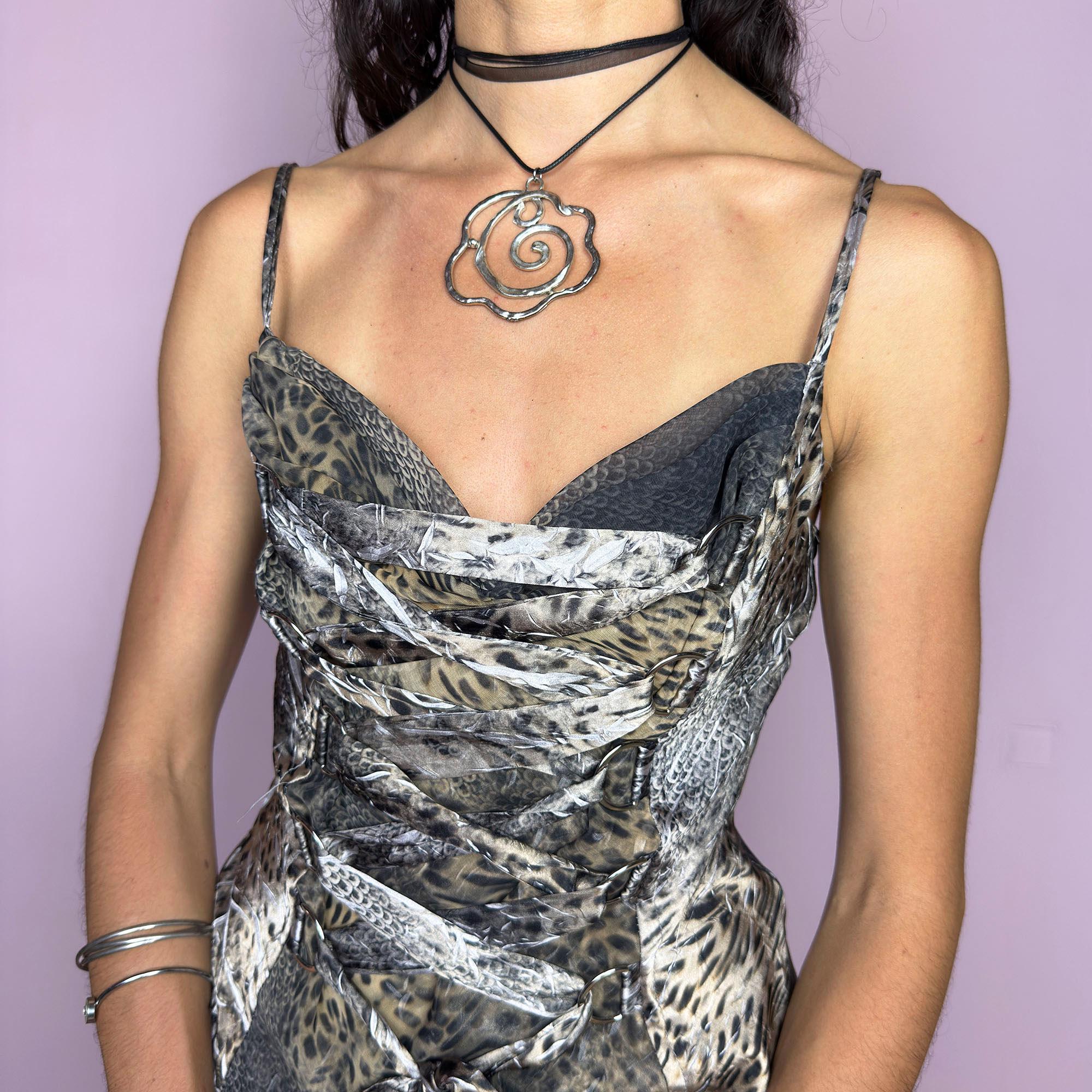 The Y2K Animal Print Corset Top is a vintage 2000s piece with a bold leopard and reptile mix print, lace-up tie front, and sculpted corset-style bodice. Featuring slim spaghetti straps and a hidden side zipper closure, this structured sleeveless top hugs the body with fierce elegance. Perfect for red carpet-inspired nights, festival glam, or a diva statement look that channels fearless Y2K energy with sensual edge. Excellent vintage condition.