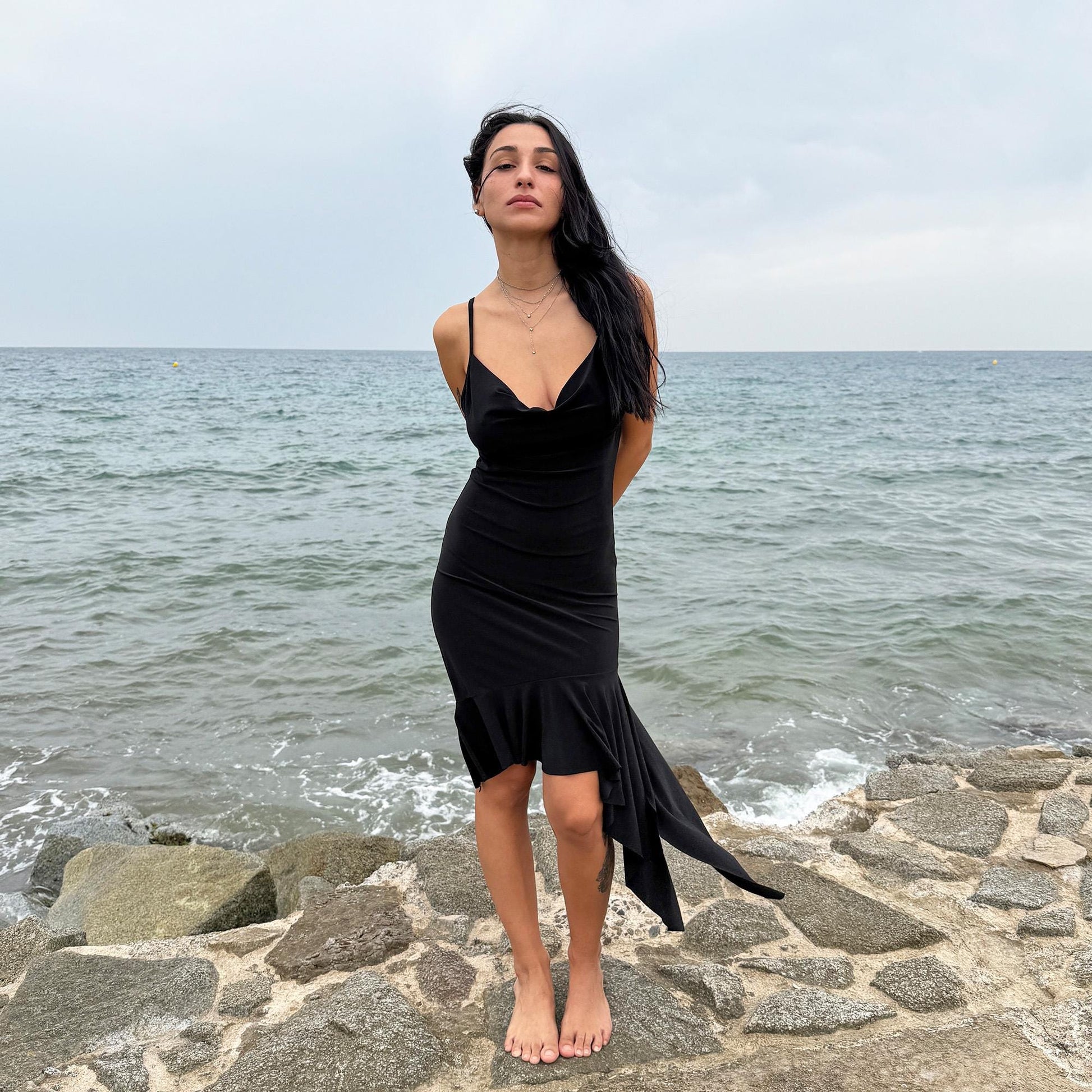 This black vintage 2000s dress features a plunging cowl neckline, and an asymmetrical ruffle hem that flutters with movement. Designed in a flattering cocktail length with a body-hugging silhouette, it’s perfect for summer nights, beach parties, or alt club looks. French-made for a dramatic, femme-fatale feel. An iconic Y2K editorial piece for minimalist seduction. Made from a polyester stretch blend. Great vintage condition.