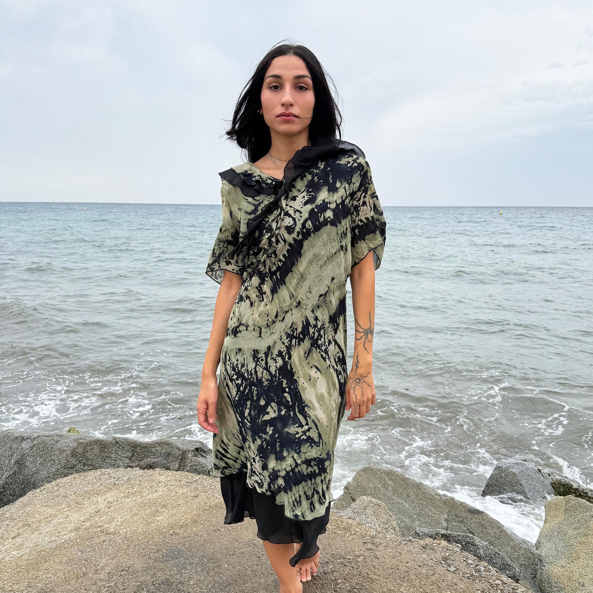 This vintage 90s midi dress features a black and green tie-dye pattern with a ruffled neckline. The short sleeves and flowy layered hem make it ideal for summer festivals, boho gatherings, or dark fairy-inspired looks. A unique Italian-made piece, perfect for forest parties or artistic styling. Made in Italy from lightweight non-stretch fabric. Excellent vintage condition.