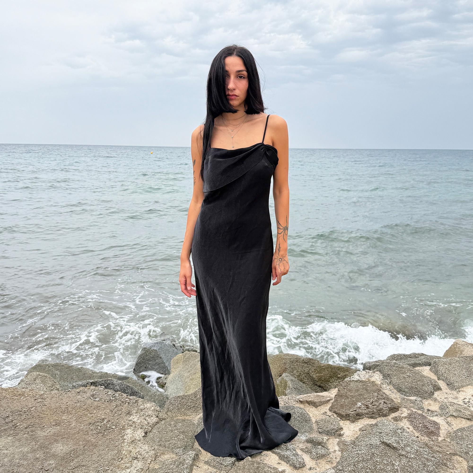 This vintage 90s slip dress in black features a lustrous finish with a straight, folded neckline and subtle ruched detailing. The fitted silhouette extends into a sleek midi length with a side zipper closure, making it ideal for evening galas, cocktail parties, or formal occasions. A stunning dark romance piece—timeless and elegant. Made from non-stretch fabric with a soft sheen. Great vintage condition.