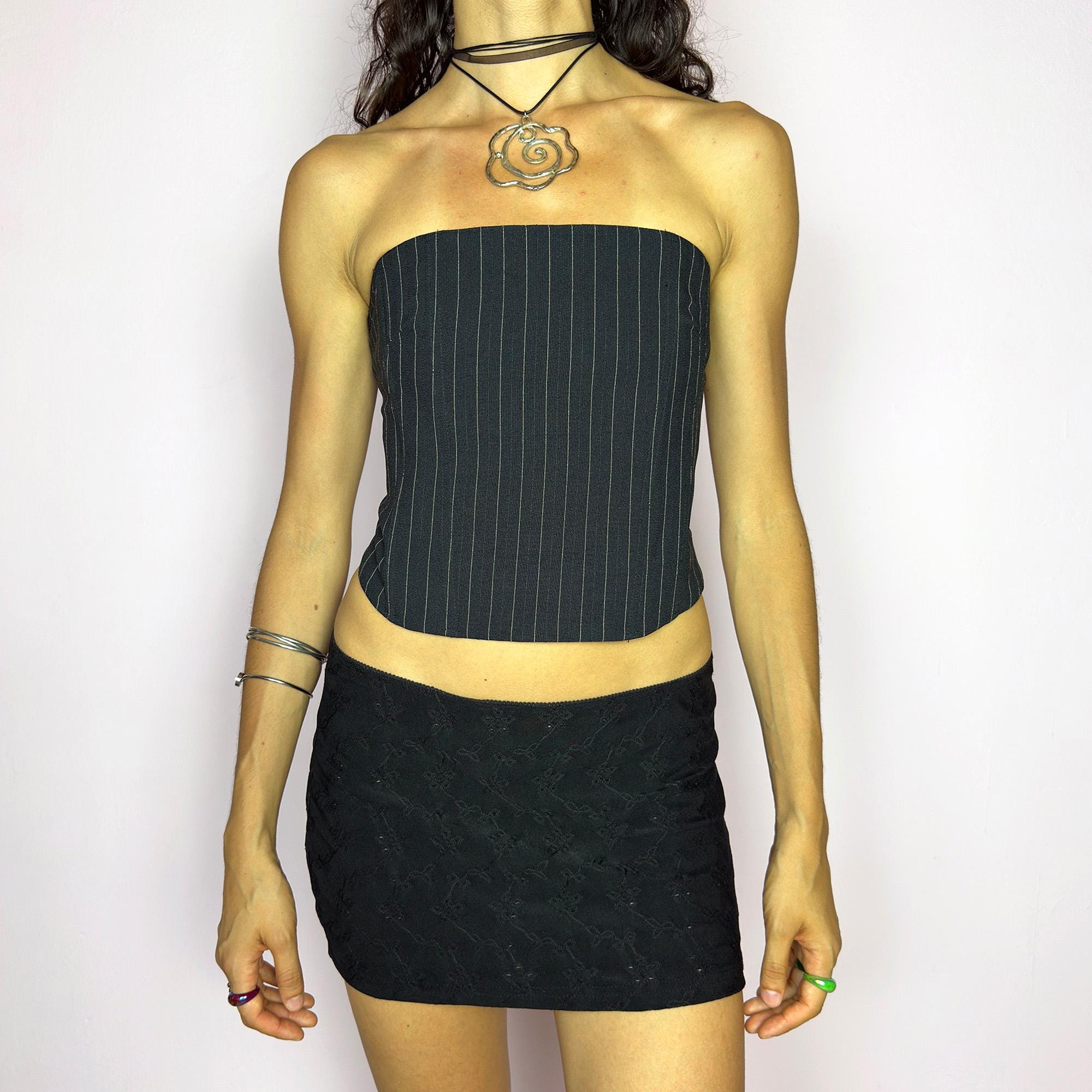 This vintage 2000s pinstripe corset top features a strapless silhouette with boning structure and a back zip closure for a sharp, tailored fit. Crafted in black with fine white stripes, it blends soft tailoring with city girl allure. Elegant yet subversive, it's ideal for cocktail hours, office party nights, or elevated downtown styling. A Y2K structured piece that channels confident, refined edge. Excellent vintage condition.