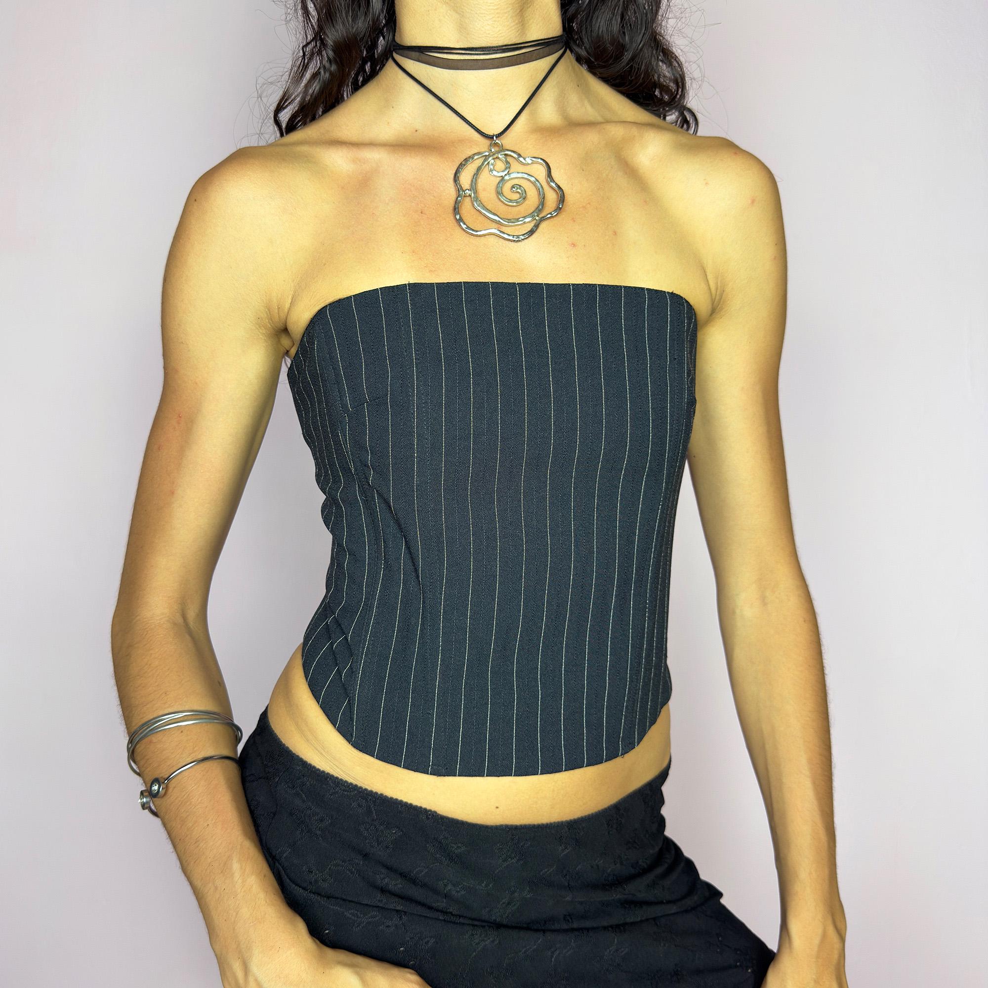 This vintage 2000s pinstripe corset top features a strapless silhouette with boning structure and a back zip closure for a sharp, tailored fit. Crafted in black with fine white stripes, it blends soft tailoring with city girl allure. Elegant yet subversive, it's ideal for cocktail hours, office party nights, or elevated downtown styling. A Y2K structured piece that channels confident, refined edge. Excellent vintage condition.