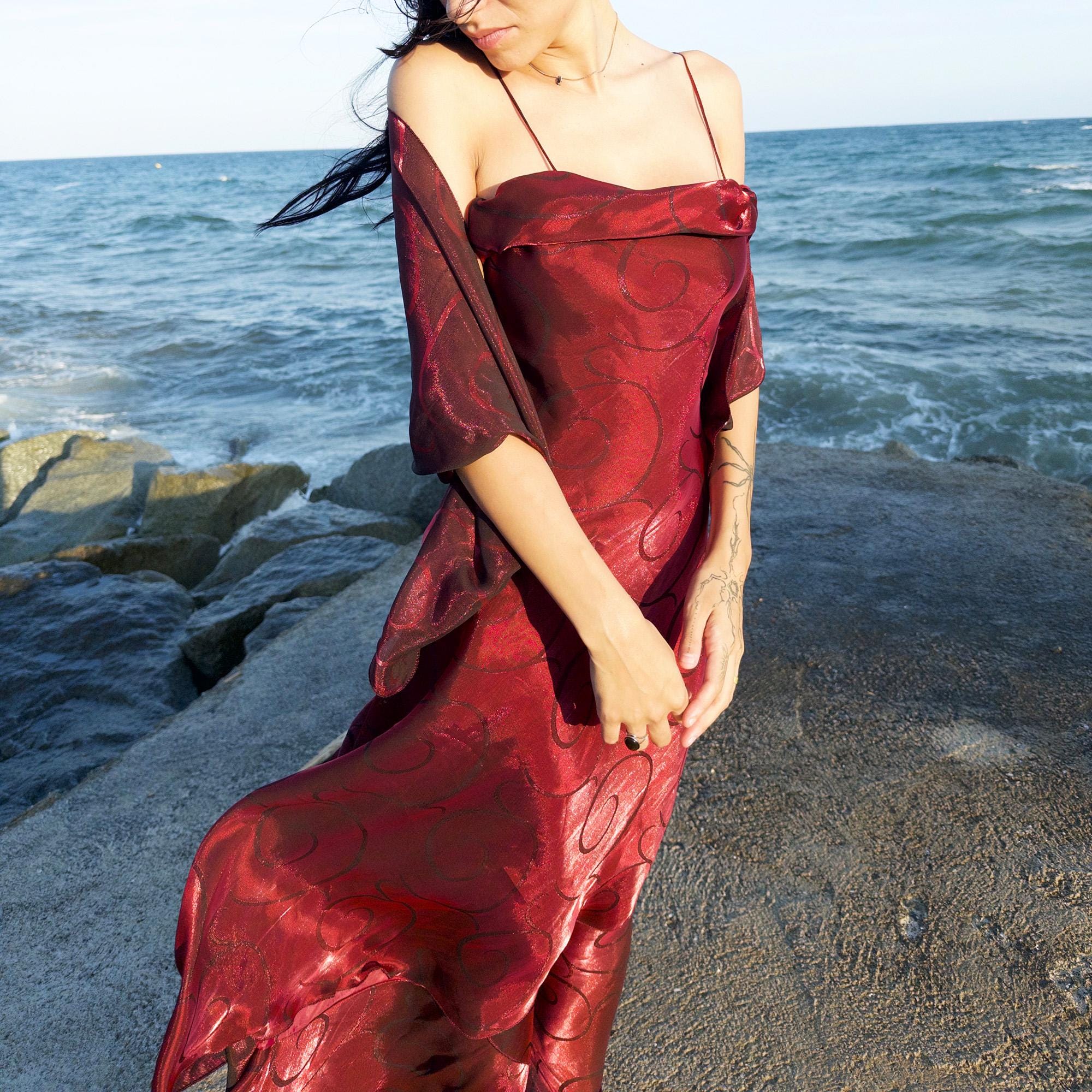 The vintage 2000s red organza-style slip midi dress is a French-made evening piece with layered maroon tones and tonal swirl pattern. With delicate spaghetti straps, side zip, and a flowing asymmetrical hem, it includes a matching scarf. Ideal for galas, proms, or romantic nights under open skies. Crafted from a semi-sheer, non-stretch fabric. Excellent vintage condition.