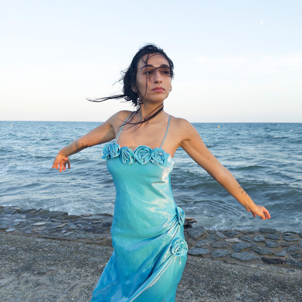 The vintage 2000s blue slip dress is a French-made fantasy with sculptural rosette appliqué along the bust and ruched side detail. Its iridescent finish and fluid midi length evoke a dreamy softness, perfect for proms, summer weddings, or romantic evenings. The silhouette is both delicate and structured, capturing quiet glamour with fairytale allure. A romantic Y2K archive crafted from a shimmering non-stretch fabric. Great vintage condition.
