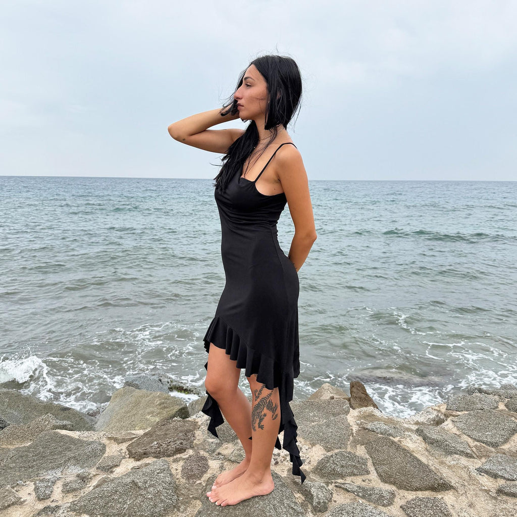 This vintage 2000s black mini dress features asymmetric straps with a subtle cowl neckline and a dramatic ruffled hem. Crafted from a stretchy fabric, it flatters the body with a bold party silhouette. Perfect for summer nights, club looks, or diva-inspired Y2K styling, this piece captures iconic 2000s glamour. Excellent vintage condition.