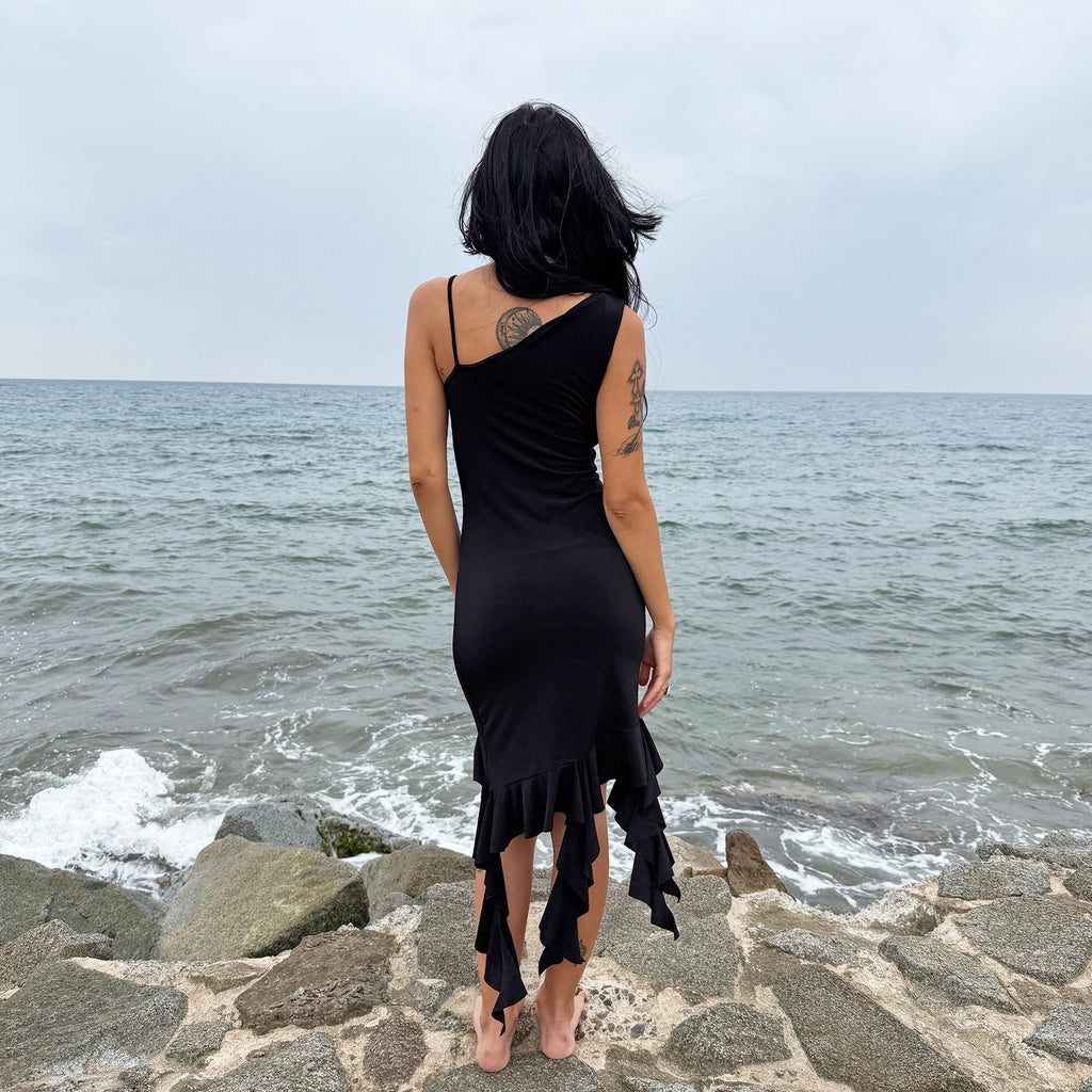 This vintage 2000s black mini dress features asymmetric straps with a subtle cowl neckline and a dramatic ruffled hem. Crafted from a stretchy fabric, it flatters the body with a bold party silhouette. Perfect for summer nights, club looks, or diva-inspired Y2K styling, this piece captures iconic 2000s glamour. Excellent vintage condition.