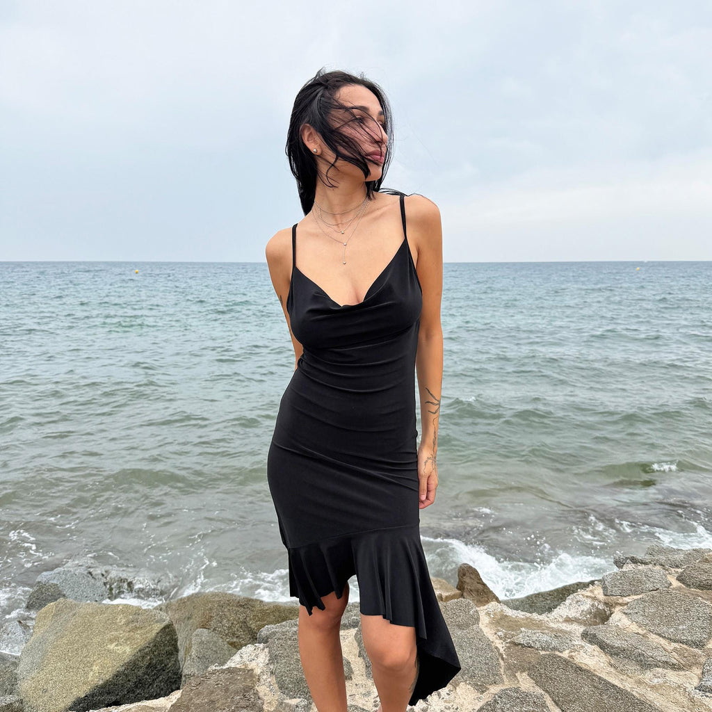 This black vintage 2000s dress features a plunging cowl neckline, and an asymmetrical ruffle hem that flutters with movement. Designed in a flattering cocktail length with a body-hugging silhouette, it’s perfect for summer nights, beach parties, or alt club looks. French-made for a dramatic, femme-fatale feel. An iconic Y2K editorial piece for minimalist seduction. Made from a polyester stretch blend. Great vintage condition.