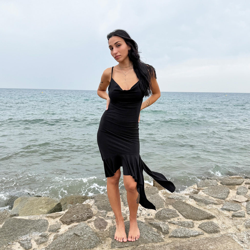 This black vintage 2000s dress features a plunging cowl neckline, and an asymmetrical ruffle hem that flutters with movement. Designed in a flattering cocktail length with a body-hugging silhouette, it’s perfect for summer nights, beach parties, or alt club looks. French-made for a dramatic, femme-fatale feel. An iconic Y2K editorial piece for minimalist seduction. Made from a polyester stretch blend. Great vintage condition.