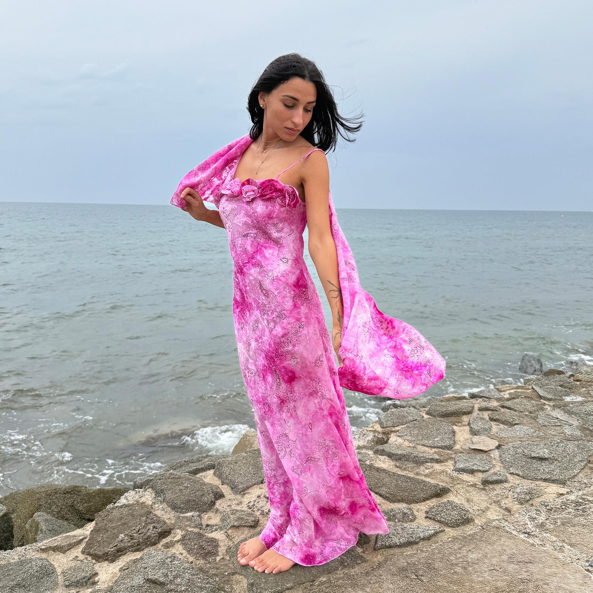 This vintage 2000s slip dress features a vivid pink tie-dye paisley print with rosette appliqué detail at the neckline. It flows into a long silhouette, ideal for summer weddings, proms, or formal parties, and comes with a matching scarf for versatile styling. A romantic archival piece made in France, perfect for bridal, evening, or statement occasions. Made from a non-stretch polyester blend. Excellent vintage condition.