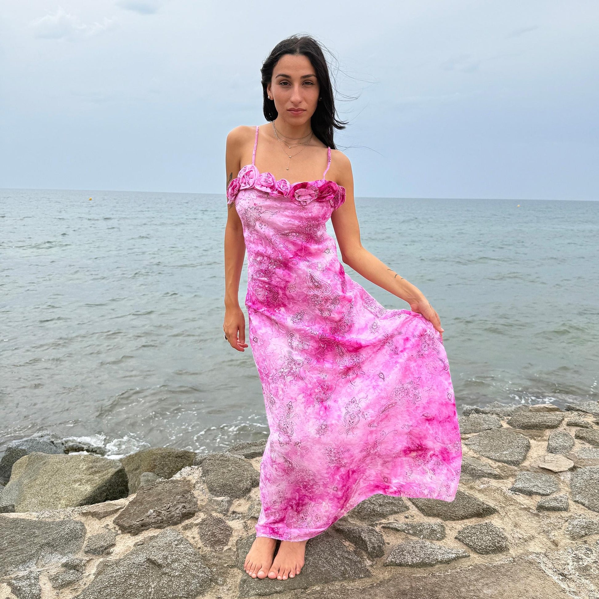 This vintage 2000s slip dress features a vivid pink tie-dye paisley print with rosette appliqué detail at the neckline. It flows into a long silhouette, ideal for summer weddings, proms, or formal parties, and comes with a matching scarf for versatile styling. A romantic archival piece made in France, perfect for bridal, evening, or statement occasions. Made from a non-stretch polyester blend. Excellent vintage condition.