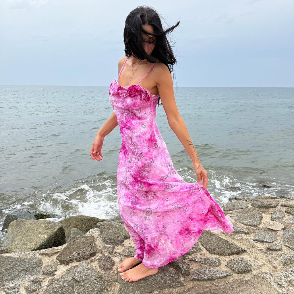 This vintage 2000s slip dress features a vivid pink tie-dye paisley print with rosette appliqué detail at the neckline. It flows into a long silhouette, ideal for summer weddings, proms, or formal parties, and comes with a matching scarf for versatile styling. A romantic archival piece made in France, perfect for bridal, evening, or statement occasions. Made from a non-stretch polyester blend. Excellent vintage condition.