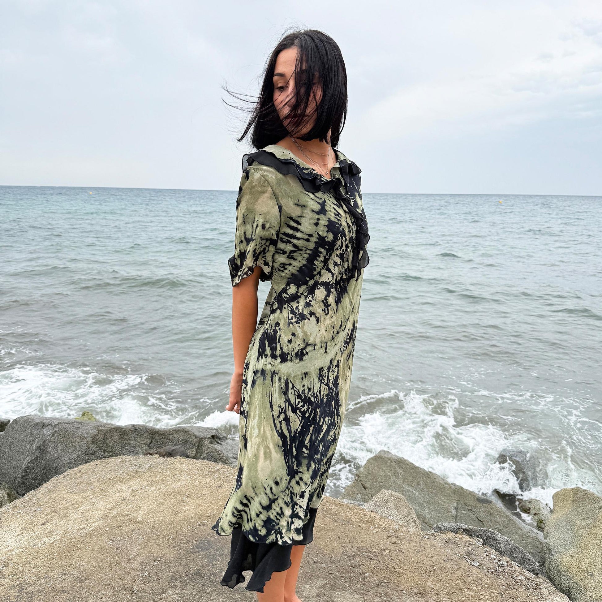 This vintage 90s midi dress features a black and green tie-dye pattern with a ruffled neckline. The short sleeves and flowy layered hem make it ideal for summer festivals, boho gatherings, or dark fairy-inspired looks. A unique Italian-made piece, perfect for forest parties or artistic styling. Made in Italy from lightweight non-stretch fabric. Excellent vintage condition.