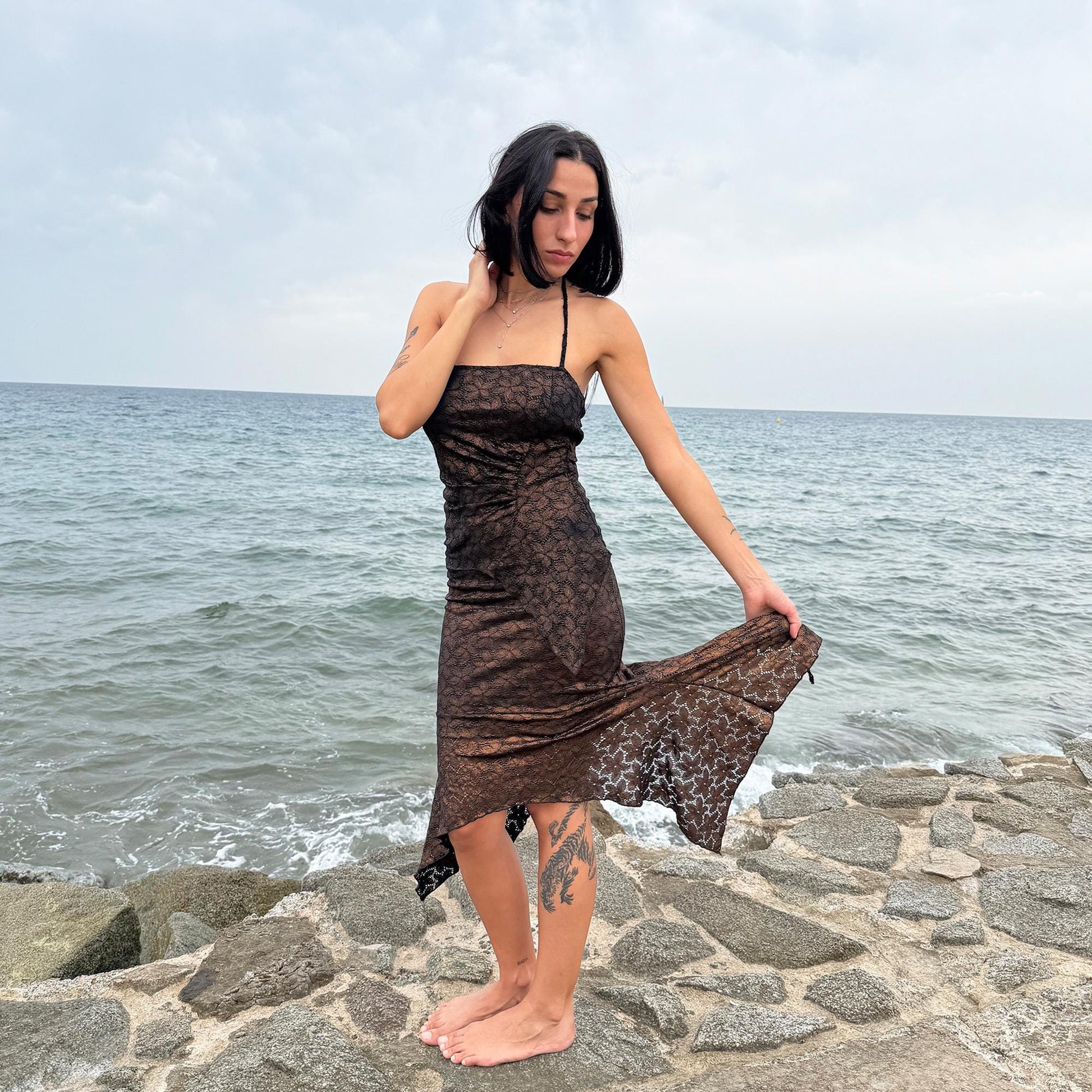 This vintage 2000s two-piece set features a shiny dark bronze-copper and black floral lace pattern. The handkerchief-style asymmetric midi skirt has an elastic waist and is paired with a matching ruched halter tie-neck top with an angled hem. A striking party set, perfect for festivals, summer nights, or dark whimsical styling. A rare archival coord for the ultimate fairy. Made in Spain from a stretchy polyester blend. Excellent vintage condition.