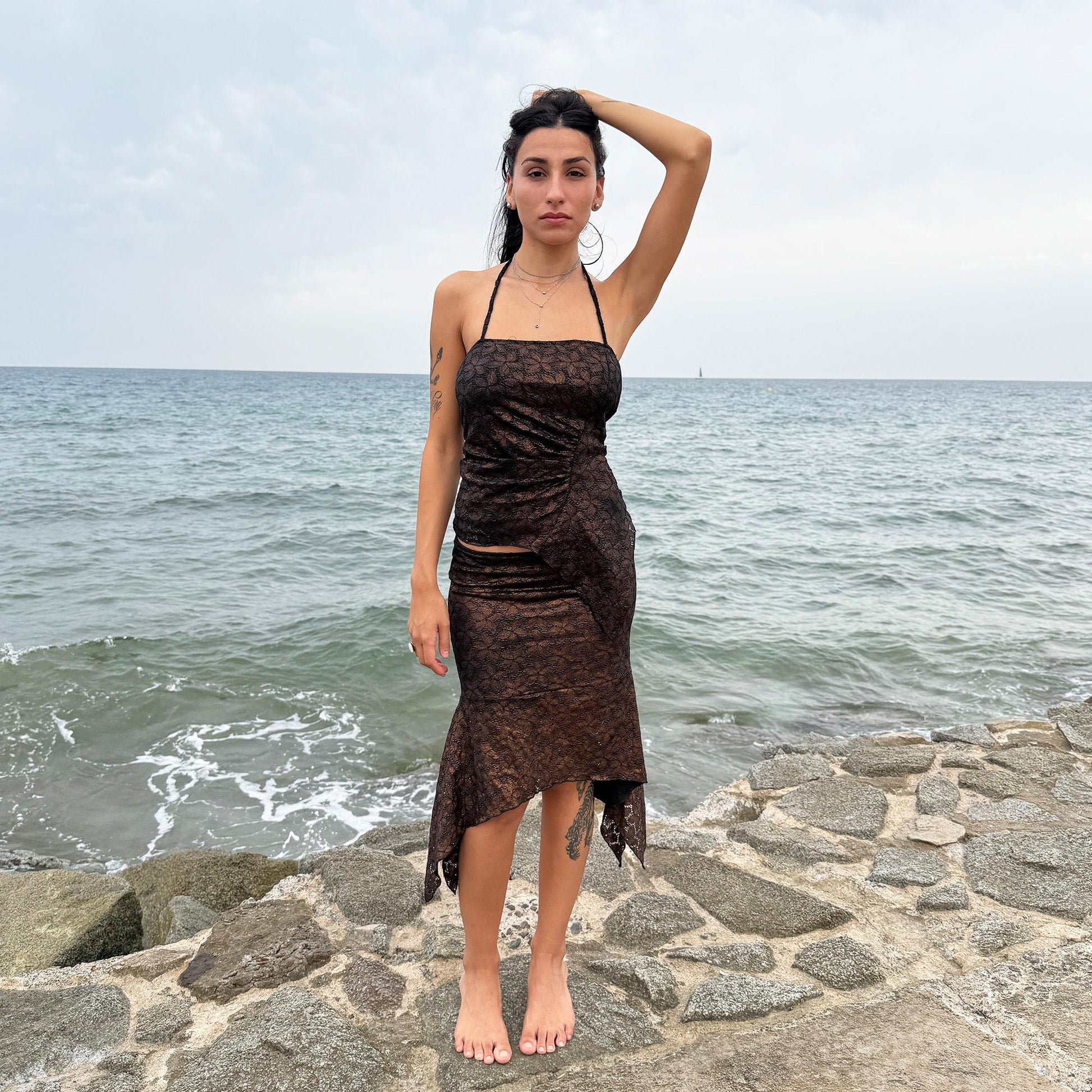 This vintage 2000s two-piece set features a shiny dark bronze-copper and black floral lace pattern. The handkerchief-style asymmetric midi skirt has an elastic waist and is paired with a matching ruched halter tie-neck top with an angled hem. A striking party set, perfect for festivals, summer nights, or dark whimsical styling. A rare archival coord for the ultimate fairy. Made in Spain from a stretchy polyester blend. Excellent vintage condition.