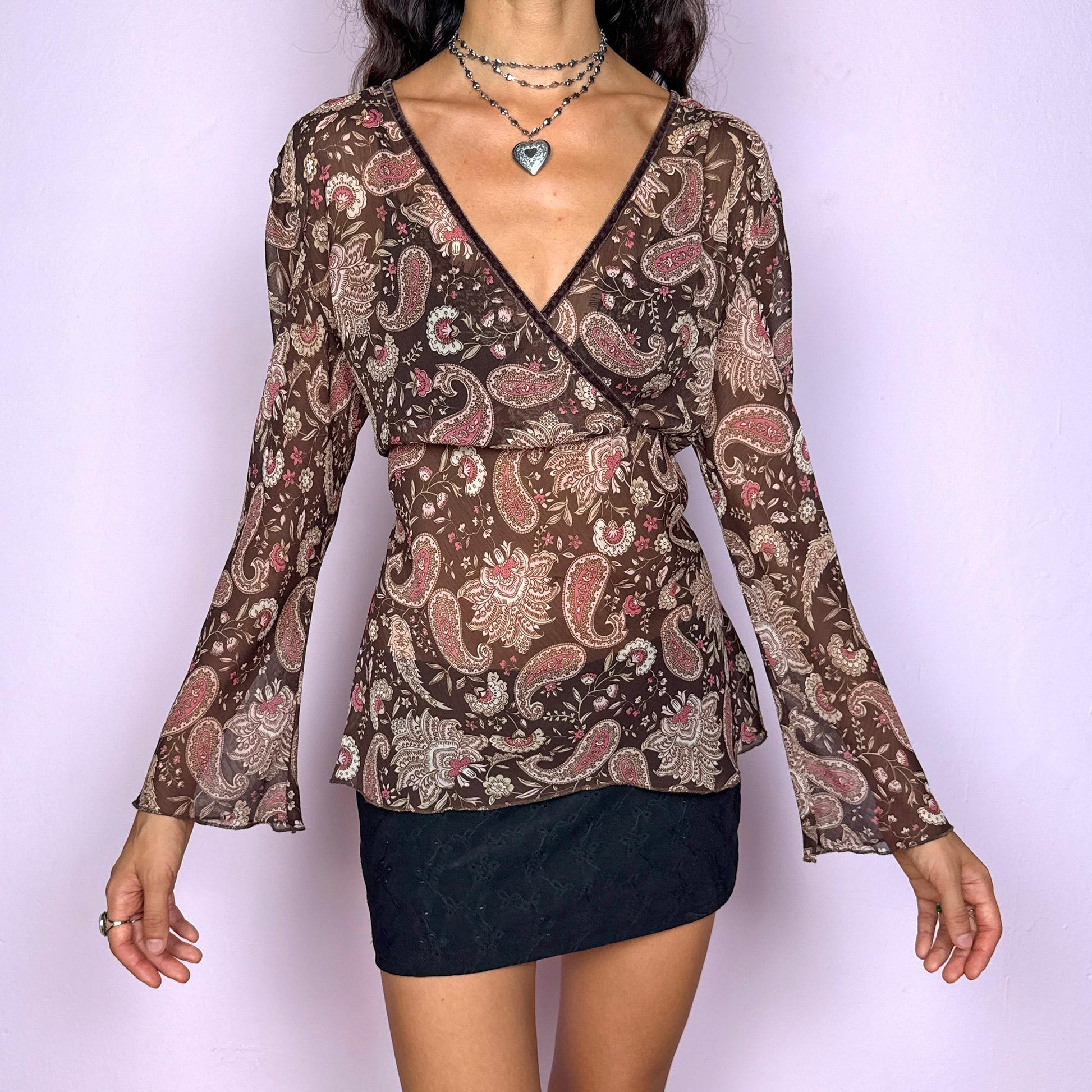This vintage 2000s paisley top features a semi-sheer brown fabric with beige and pink accents. Designed with a wrap V-neckline and flowing bell sleeves, it balances boho romance with Y2K edge. Perfect for spring and summer events, styled over a bikini, or layered for night outings with a hippie-chic aesthetic. Great vintage condition.