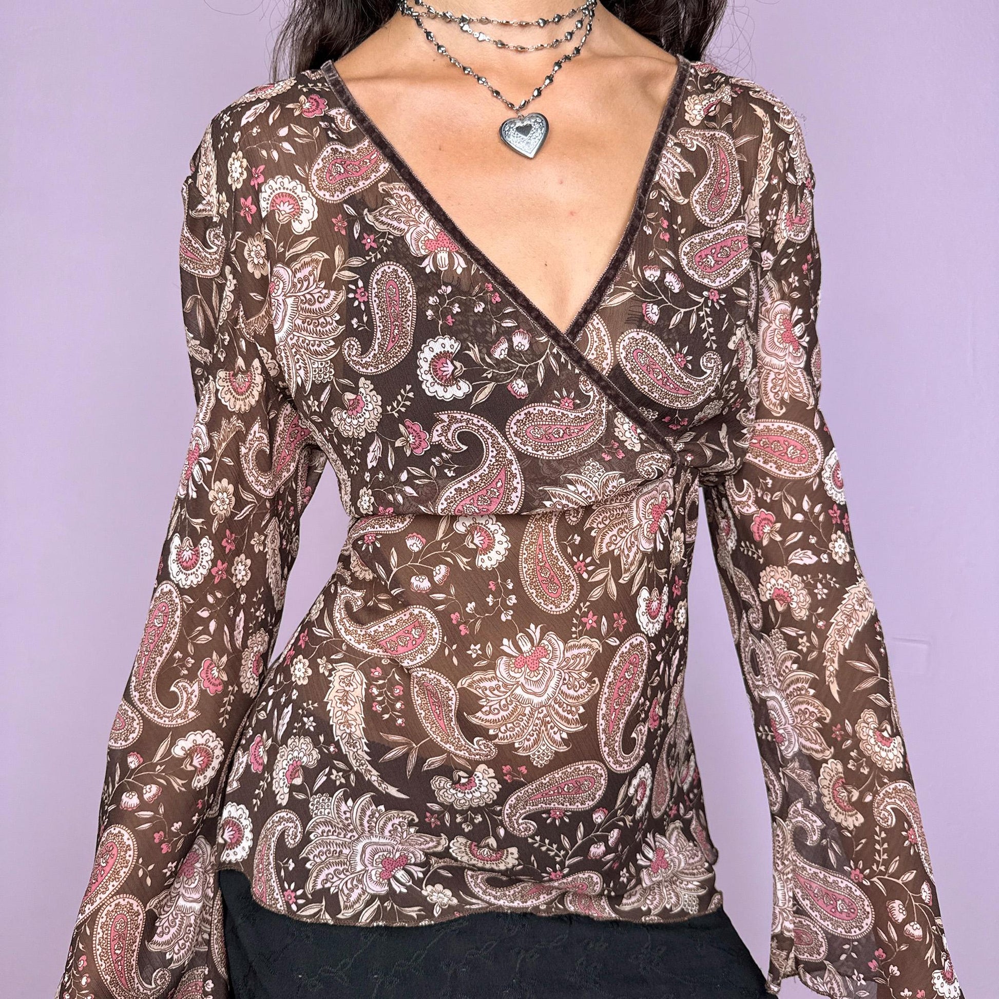 This vintage 2000s paisley top features a semi-sheer brown fabric with beige and pink accents. Designed with a wrap V-neckline and flowing bell sleeves, it balances boho romance with Y2K edge. Perfect for spring and summer events, styled over a bikini, or layered for night outings with a hippie-chic aesthetic. Great vintage condition.