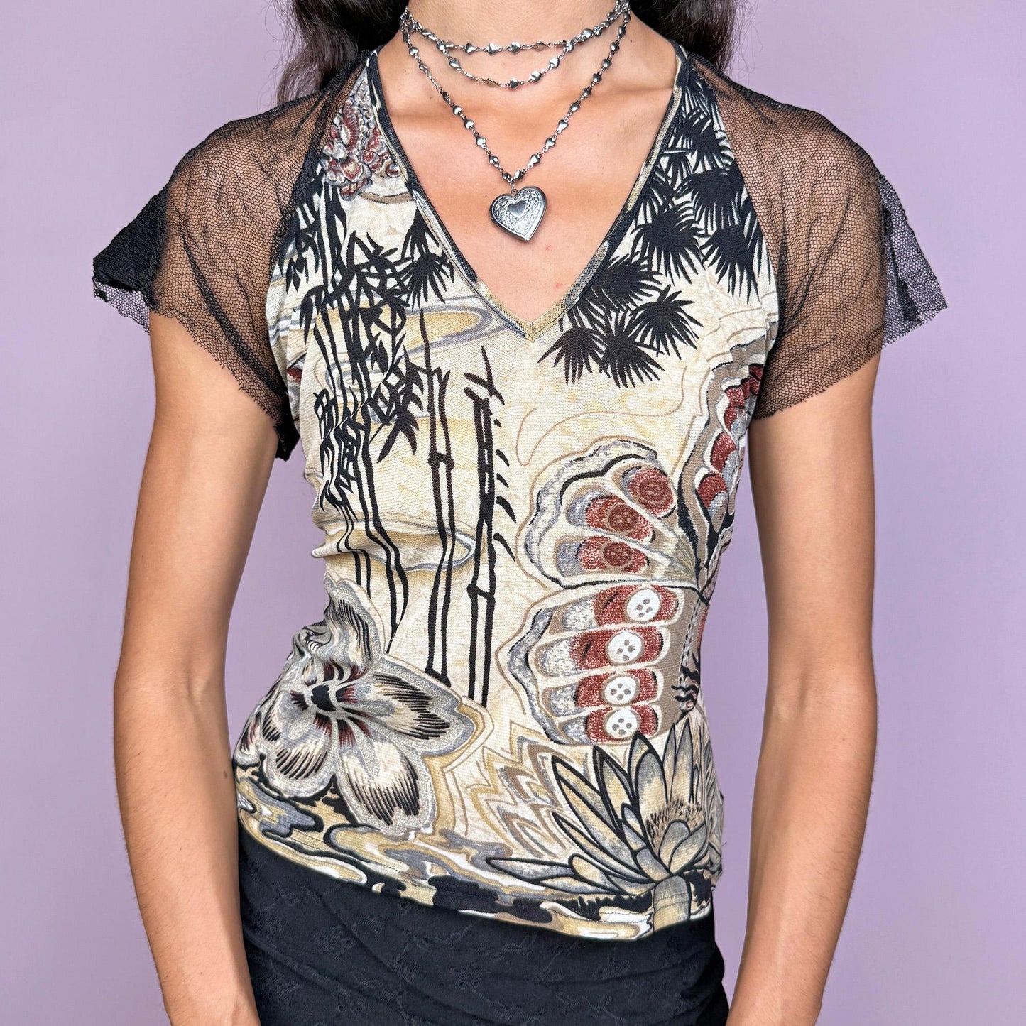 This vintage 2000s top features a bold bamboo and lotus print on the front in cream/beige, black, and rust tones, contrasted by a sheer black lace back with a butterfly pattern. Designed with short mesh sleeves and a fitted cut, this artistic piece is made for after-dark layering or statement summer styling. A rare editorial piece with deconstructed energy. Made from a polyester stretch blend. Excellent vintage condition.
