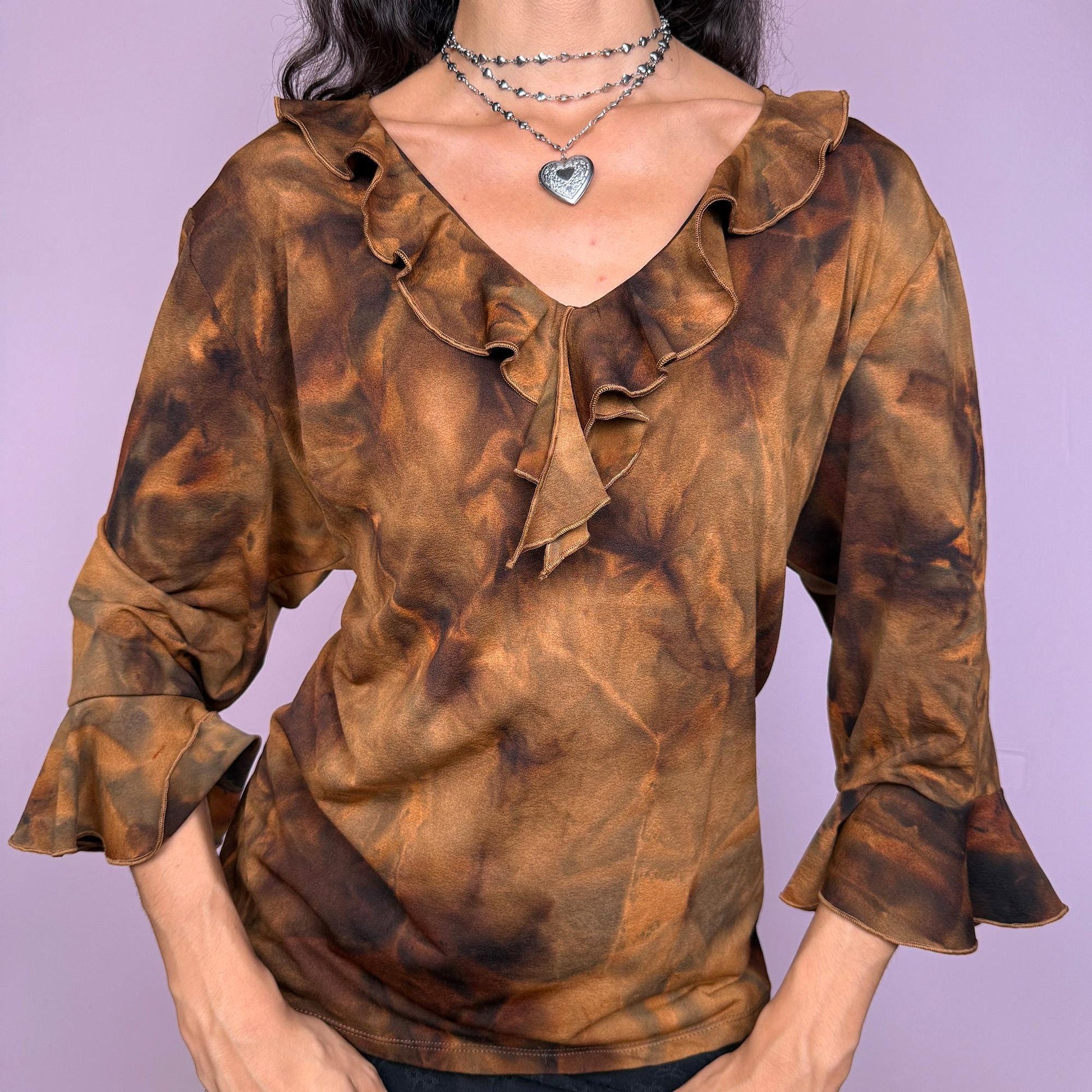 This vintage 2000s brown tie-dye top features a ruffle neckline and three-quarter bell sleeves. Made from stretchy fabric, it channels fairycore with earthy depth and whimsical structure. A perfect piece for boho layering, festival nights, or forest-inspired edits. Made in Spain from a polyester blend. Excellent vintage condition.