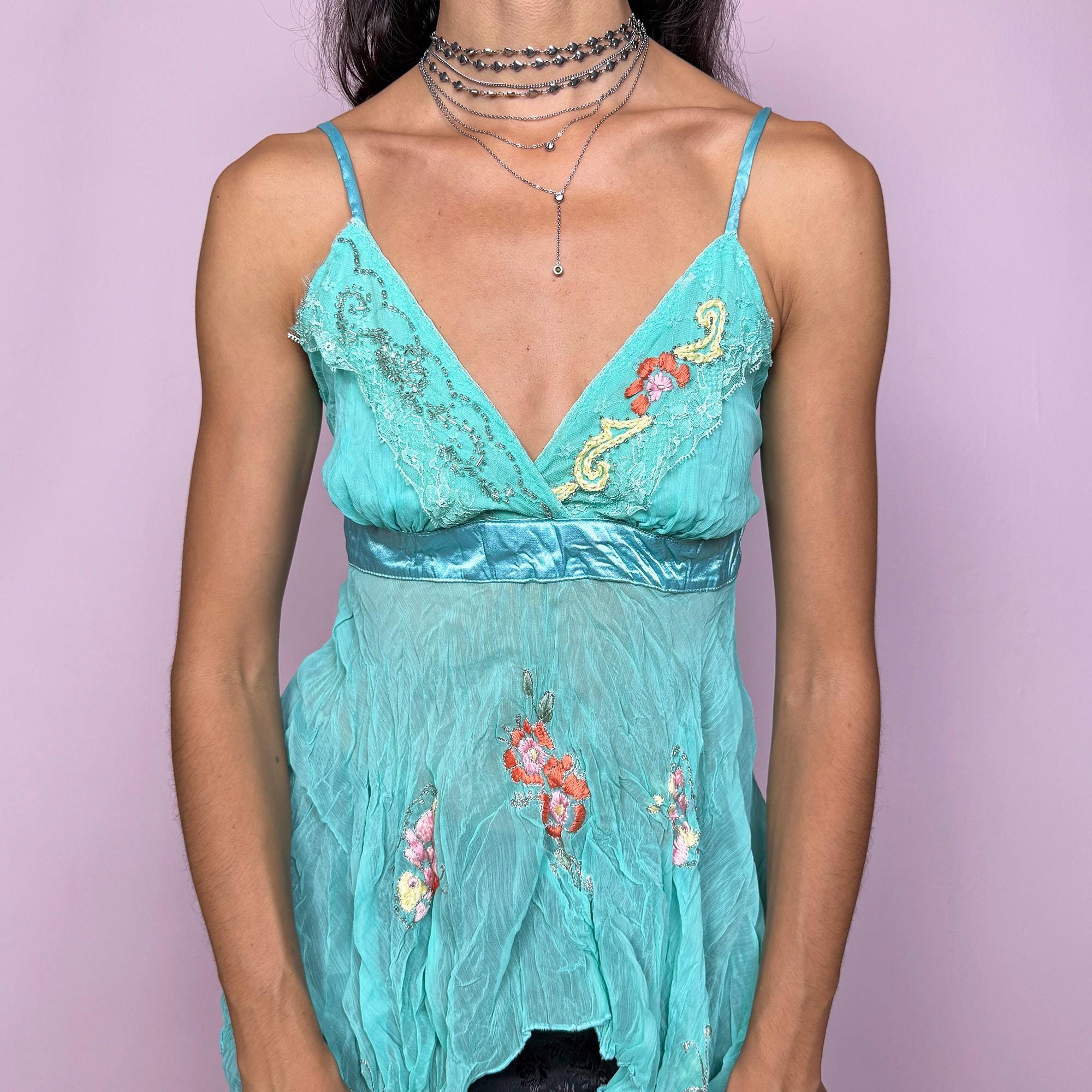 This vintage 2000s pastel turquoise cami top features exquisite floral embroidery and delicate beaded detailing over a sheer body. Designed with adjustable straps, a back zipper closure, and an asymmetric handkerchief hem, it captures ethereal movement and sensual Y2K charm. A romantic, whimsical piece made for summer nights, parties, and layered editorial styling. Made from non-stretch polyester. Excellent vintage condition.