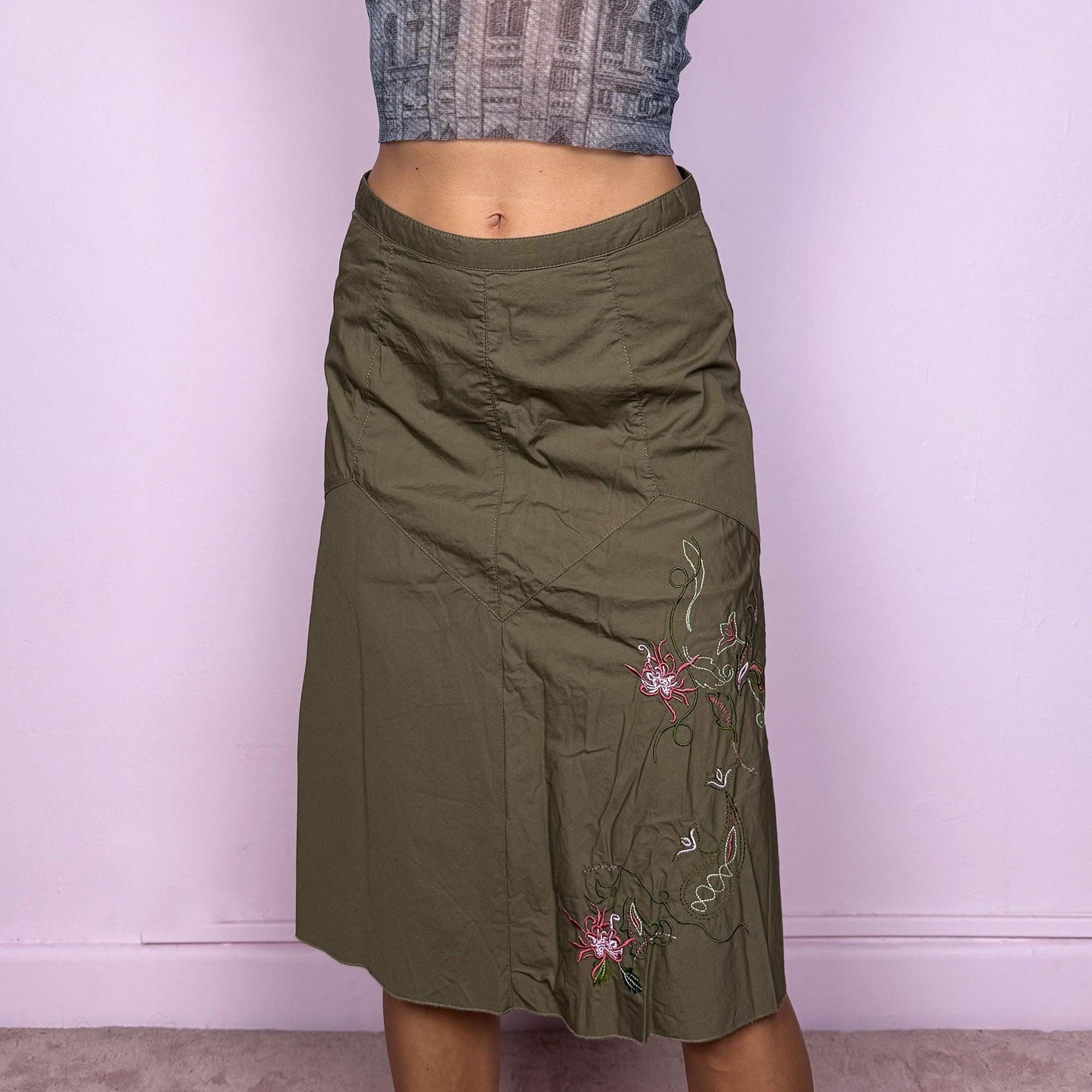 This vintage 2000s khaki green midi skirt features a soft flared silhouette with floral embroidered details and a back zipper closure. Made from cotton, it’s flowy, breathable, and perfect for summer or office wear. It can be styled low-rise on XXS or mid/high-rise on XS, offering versatile fit and effortless elegance. Excellent vintage condition.